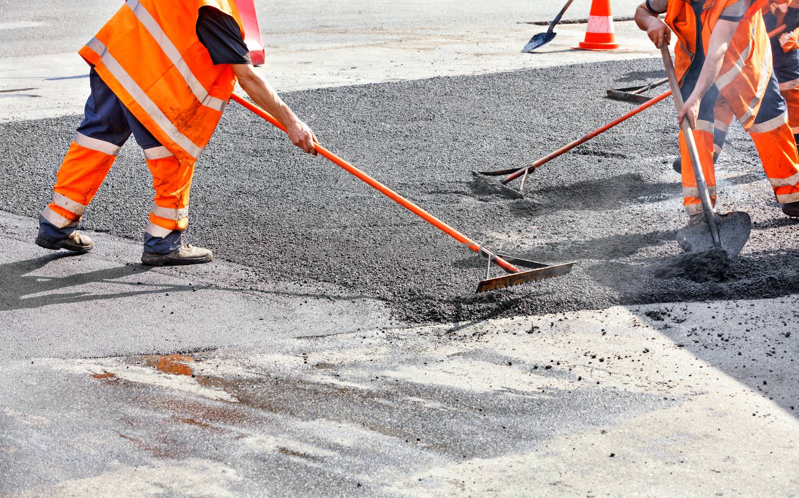 The working team smoothes hot asphalt with a metal levels and shovels by hand when repairing the road. by Sergii