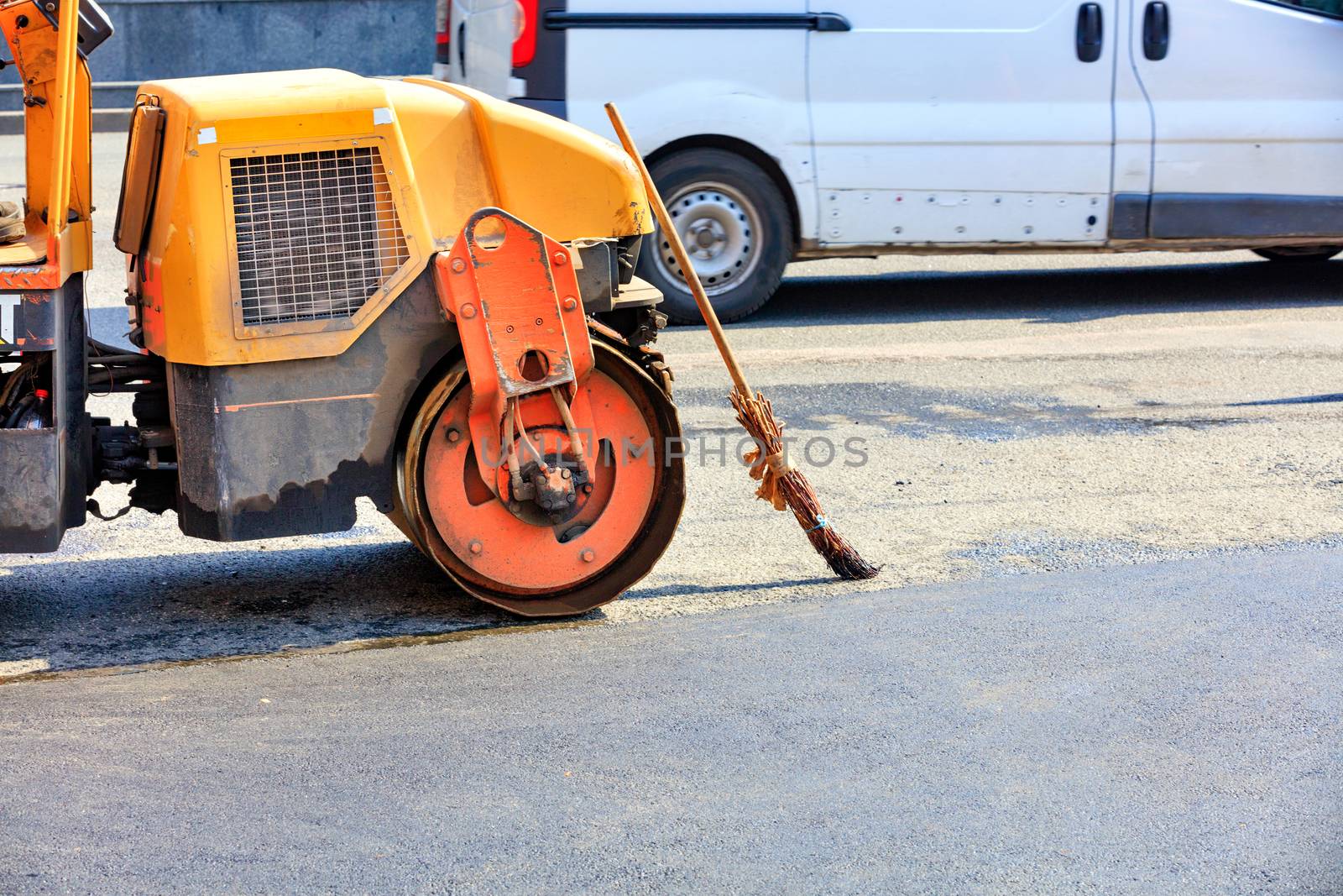 An old gasoline vibratory skating rink and an old broom are standing near a repaired section of the carriageway. by Sergii