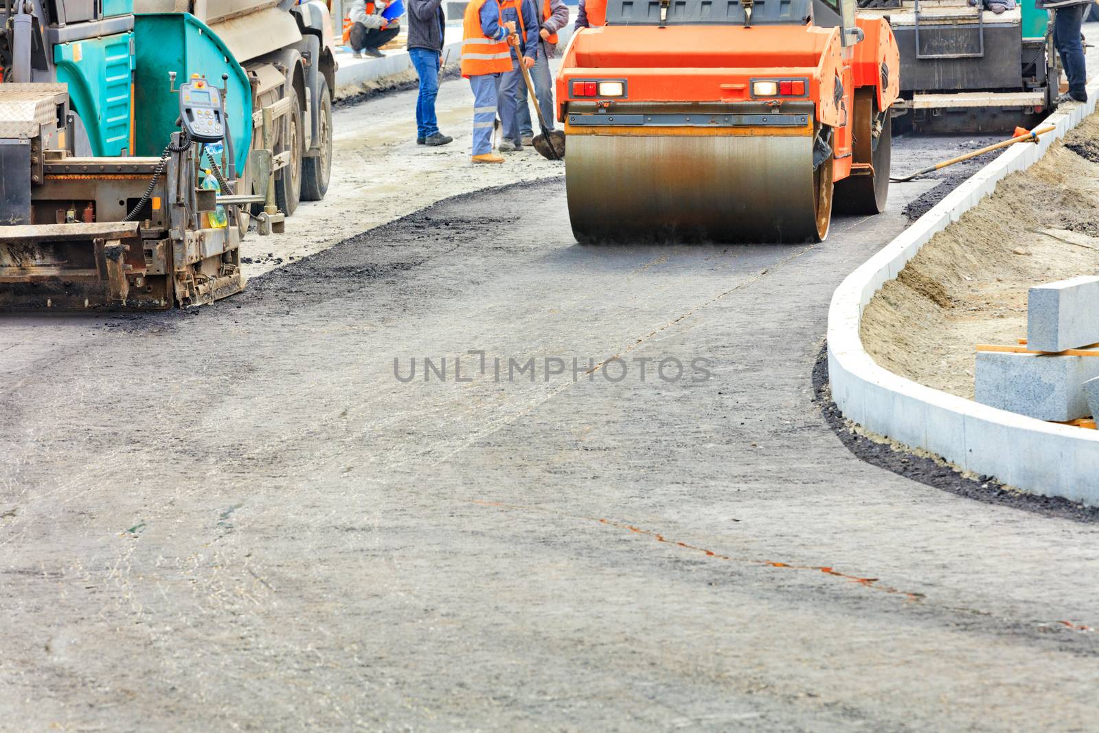 Heavy road equipment, such as pavers and a road vibratory roller, are serviced by a road maintenance team to build new transport routes.