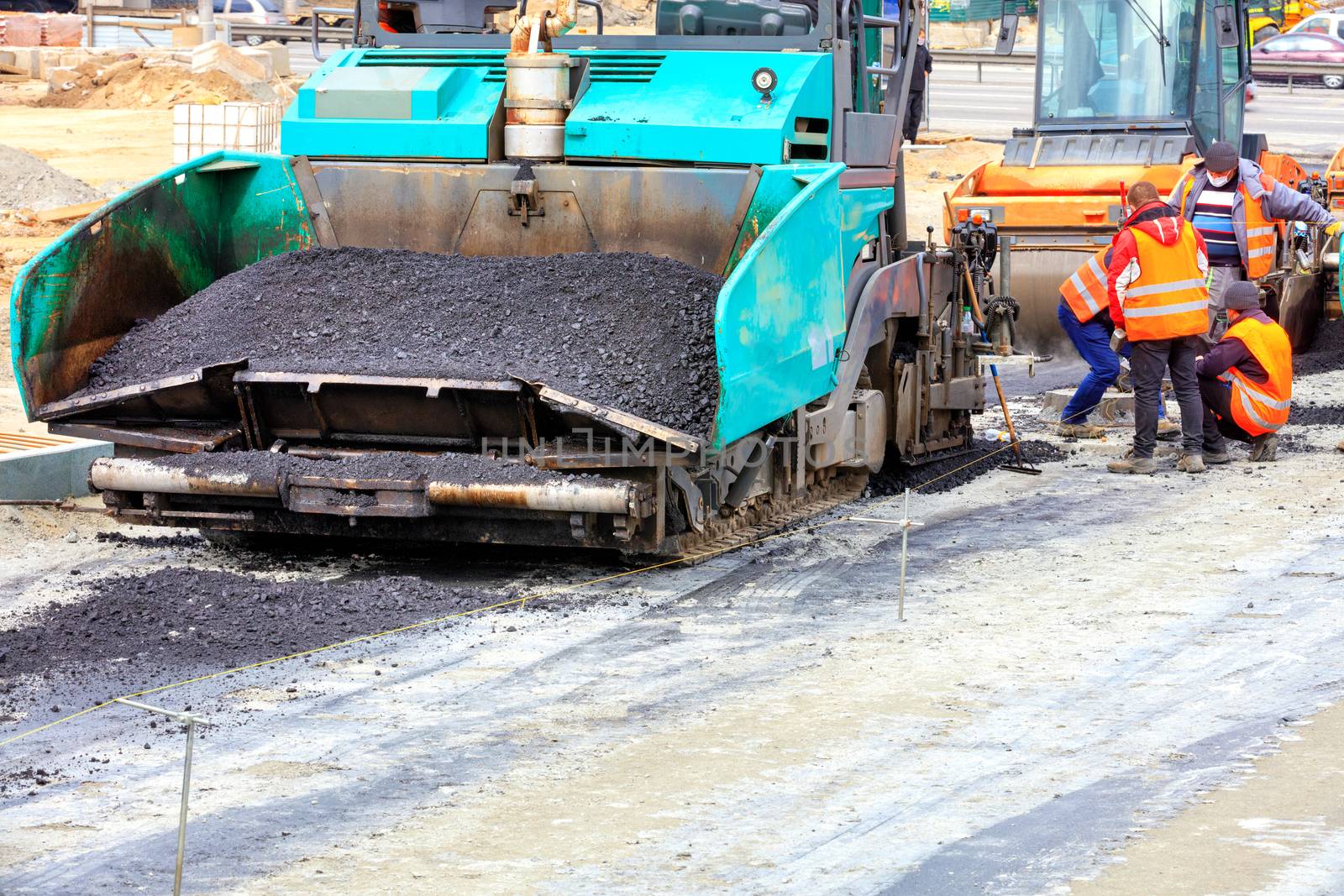 The large asphalt paver is filled with fresh asphalt in the foreground and the road vibratory roller is waiting for the construction of a new asphalt road, copy space.