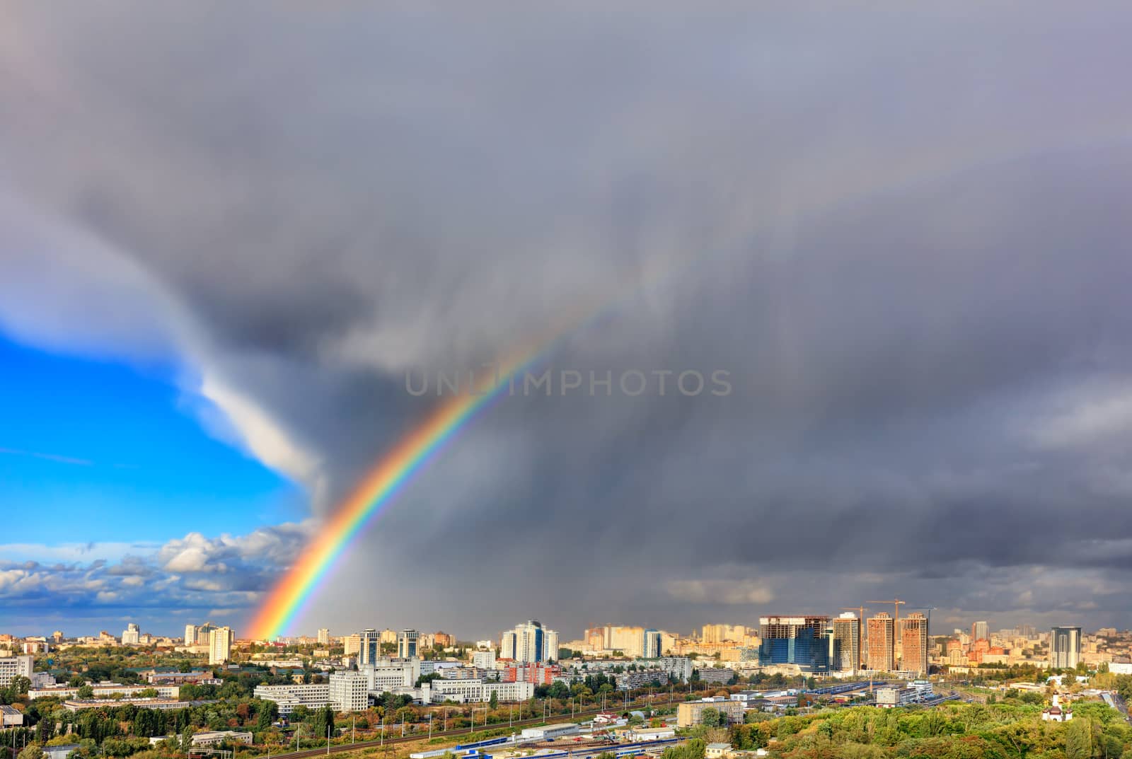 A bright rainbow in the sky above urban houses, sunlight displaces a thunderous front revealing a blue sky. The concept of change for the better.