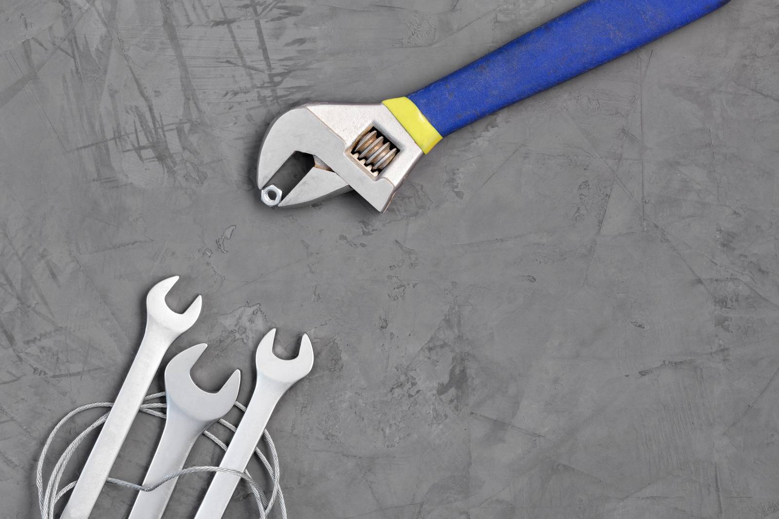 The adjustable wrench in the blue handle provides food for new wrenches on a background of gray concrete. The concept of training for workers and development, copy space, place for text.