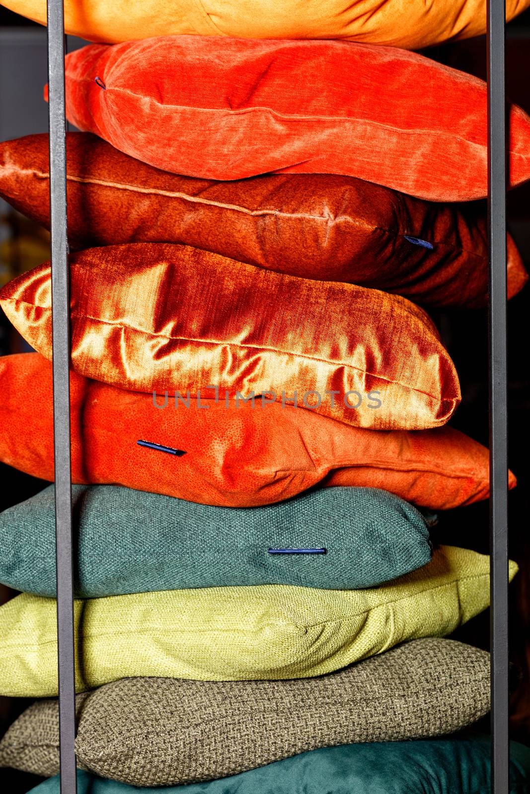 Collection Red, orange, yellow, green, terracotta shades of textile stacks of decorative pillows on a dark background with a metal frame.