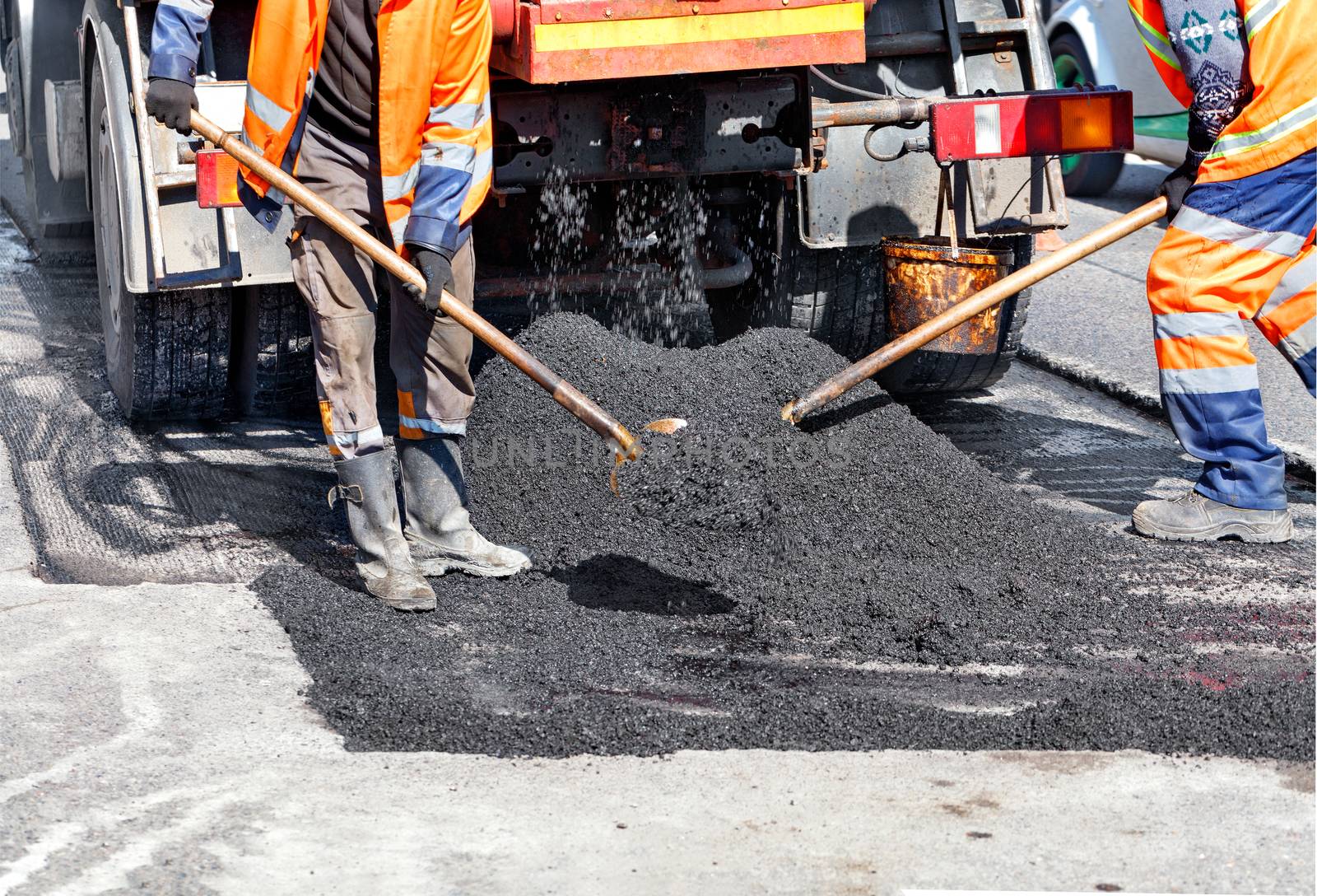 The working group of road workers with shovels updates part of the road with fresh asphalt to update it in road construction, place for text, copy space.