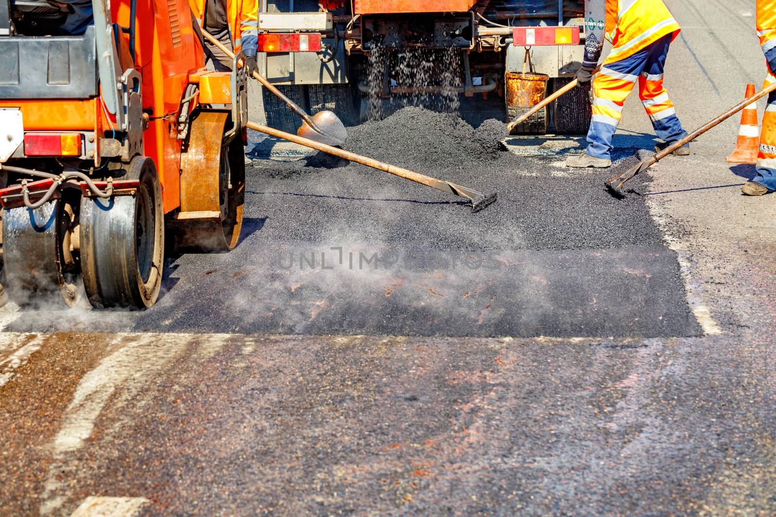 A team of road workers in protective orange overalls repairs a section of the road using shovels, levels and small road equipment, copy space.