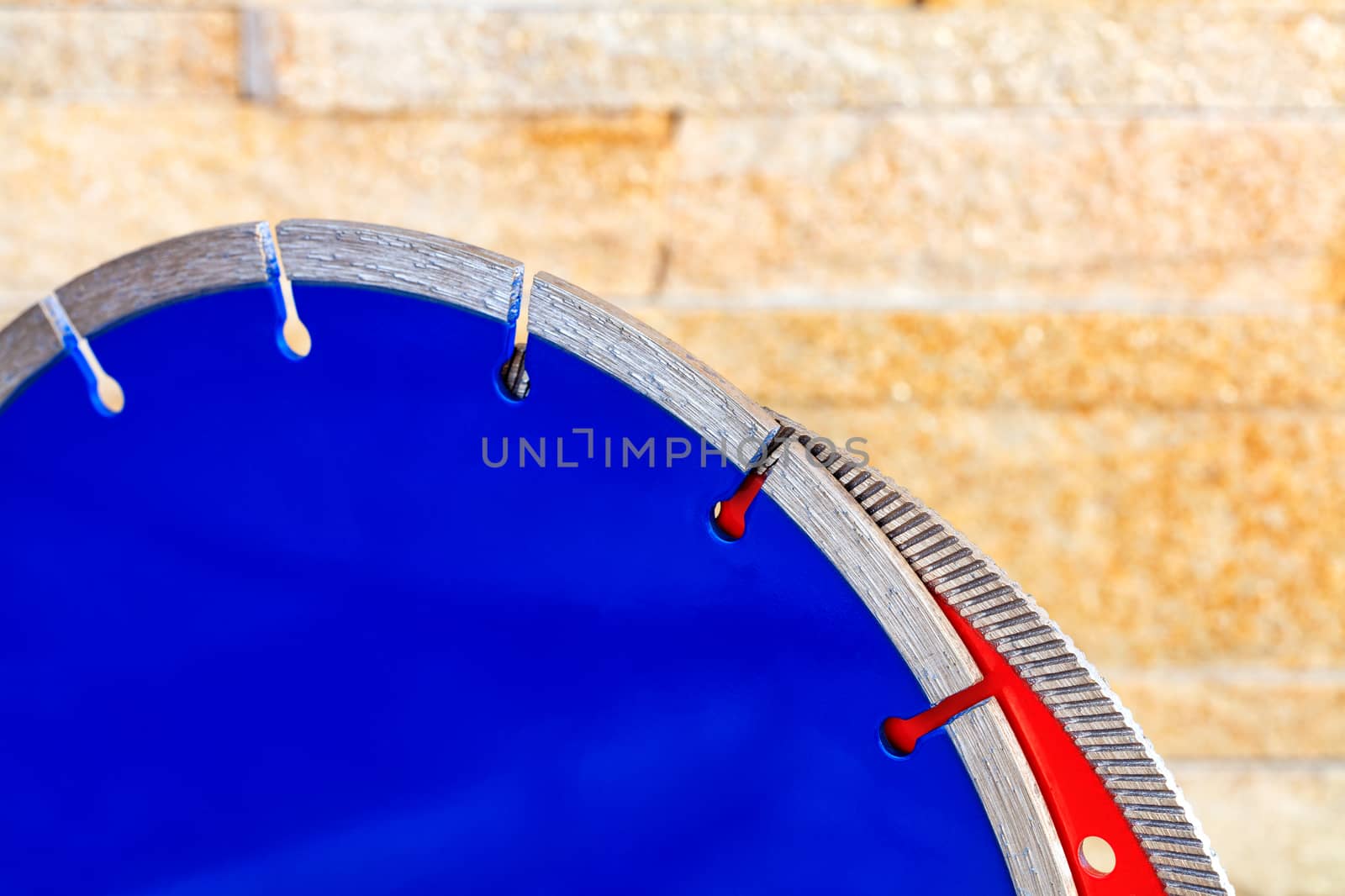 Blue diamond cutting disc for concrete, red for granite, close-up of cutting segments on the background of an orange sandstone wall in blur, copy space.