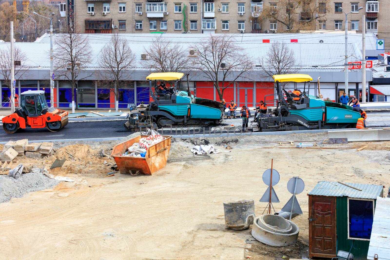 Kyiv, Ukraine, 03/28/2020. Large pavers and a road vibratory roller go one after another on the construction of a new traffic intersection. by Sergii