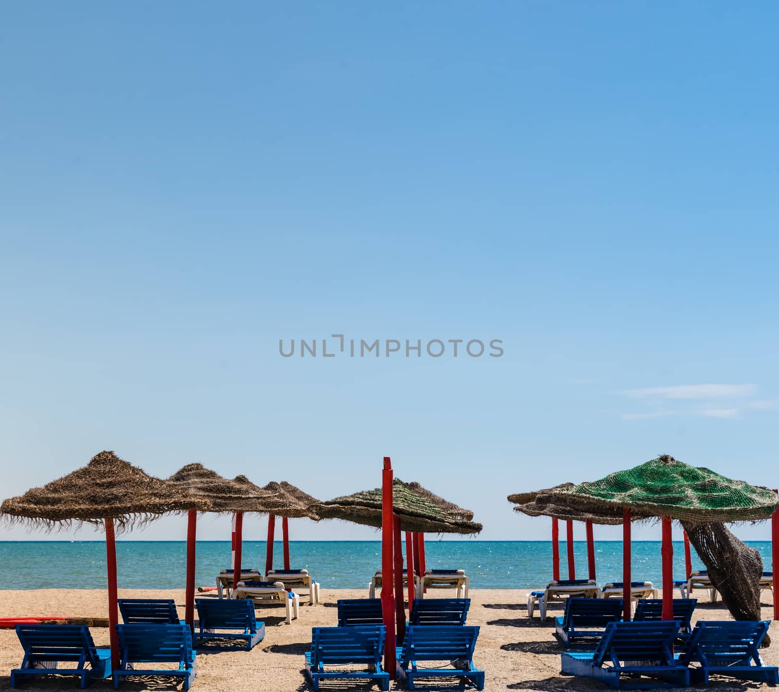 Lonely wicker sun umbrella with two hammocks on empty beach in Fuerteventura. Colorful turquoise sea water on sunny day in Caleta de Fuste, Canary Islands. Nobody enjoying summer holidays concept by jcdiazhidalgo