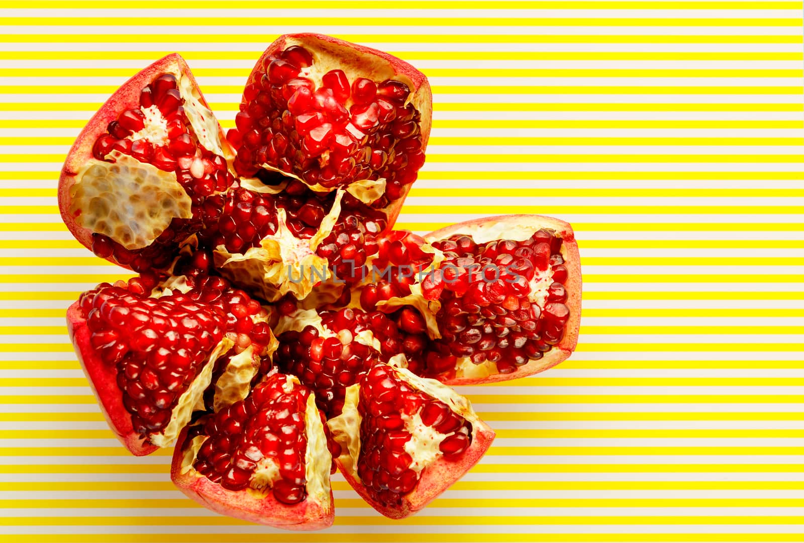 Ripe and red pomegranate fruits and are divided into parts, on a striped yellow background, close-up, copy space, top view.