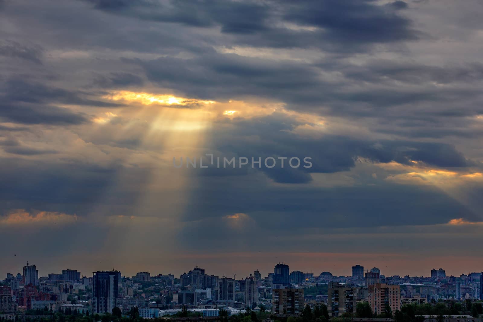 The sun's rays break through dense clouds at dawn over a sleeping city. Shining light in the dramatic morning sky.