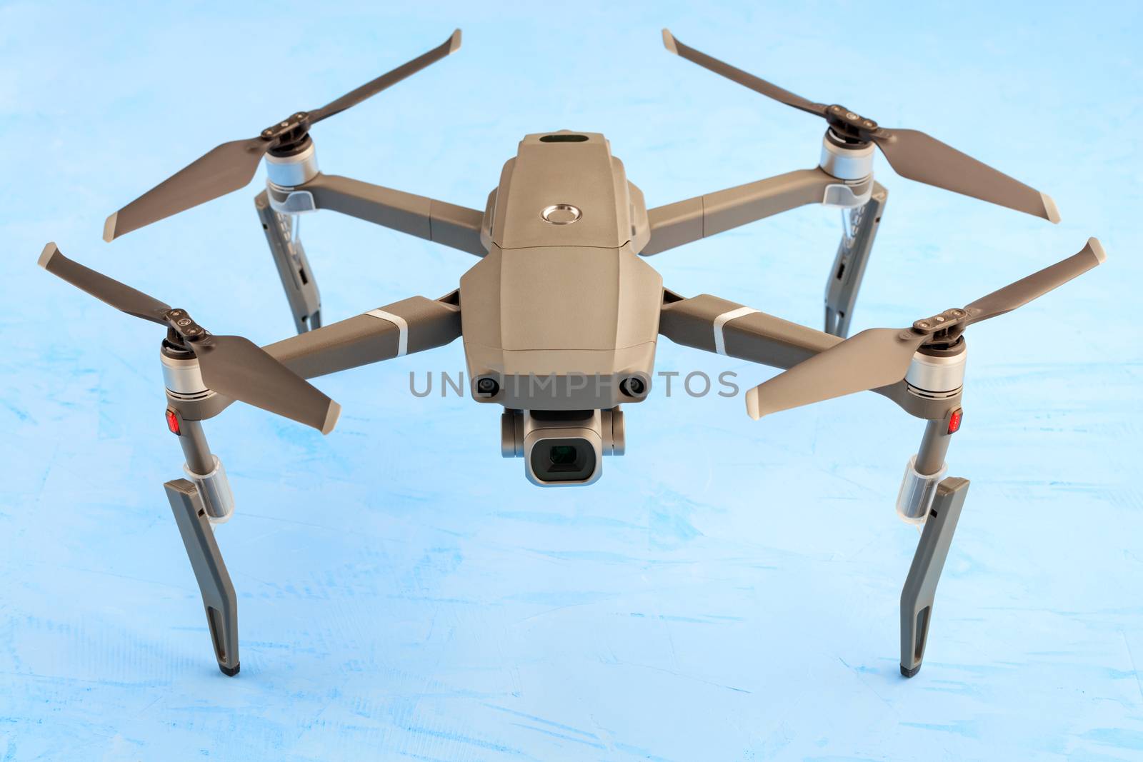 A model of an unmanned quadrocopter with an enlarged landing gear and cardan shock absorbers on a blue surface with a high-resolution camera installed. This is a new technology for aerial photography and video.