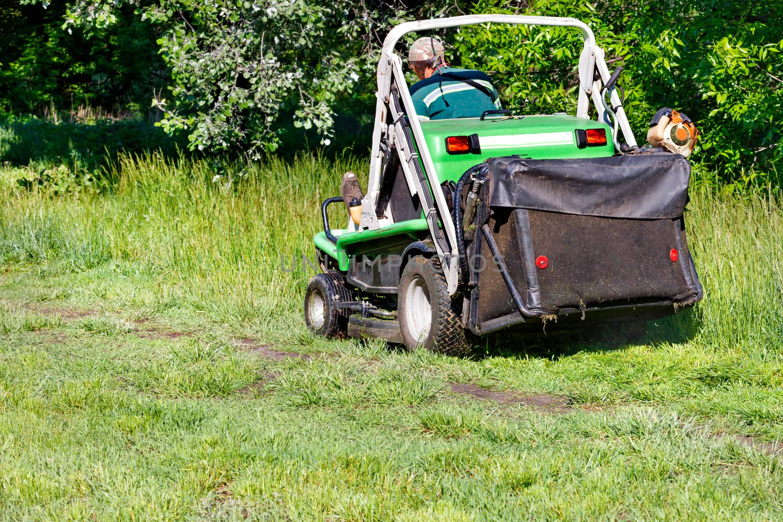 A utility service worker mows tall grass in an overgrown garden with a professional lawn mower on a clear sunny day, copy space.