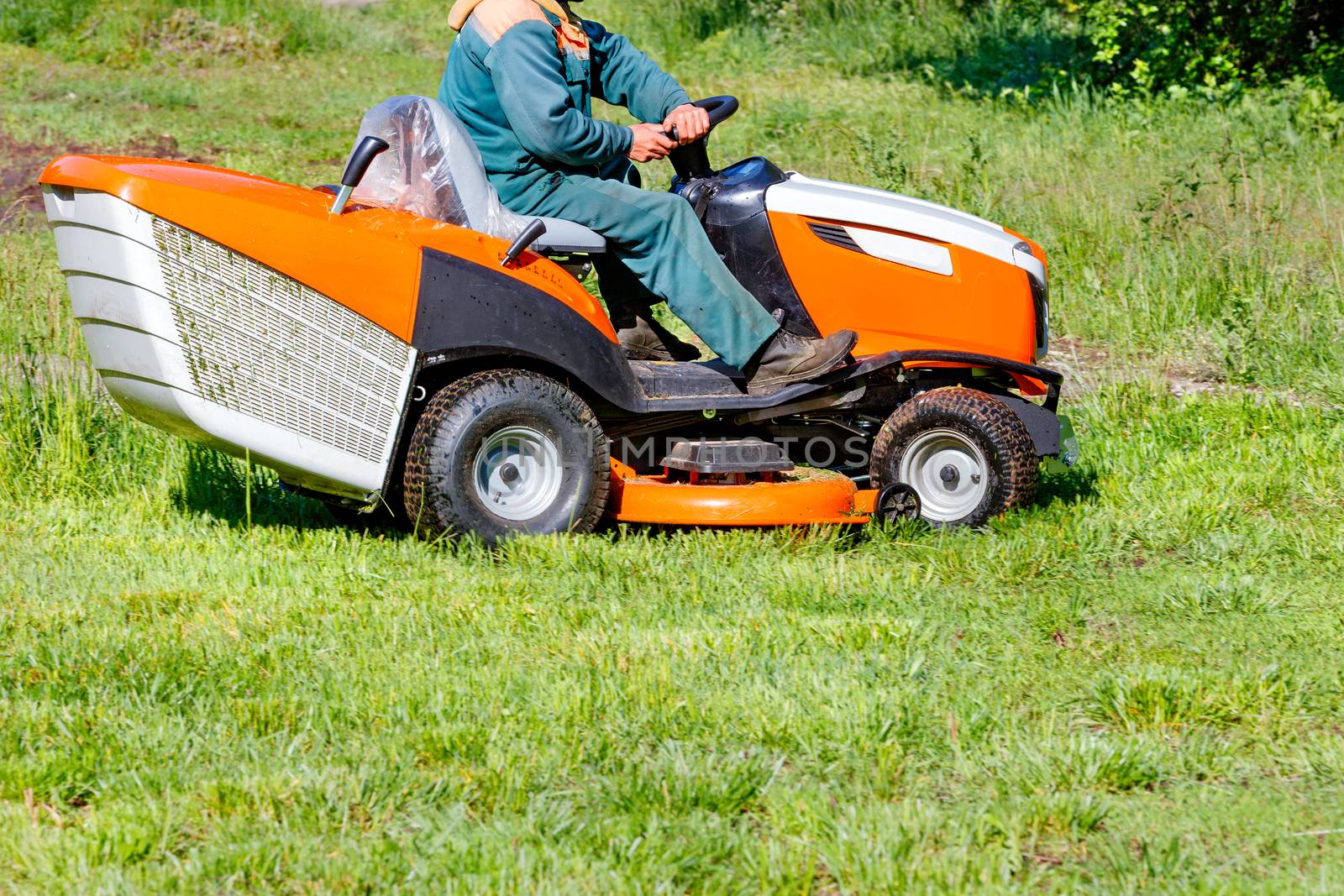 A service worker mows grass on the lawn with a professional lawn mower on a clear sunny day, copy space.