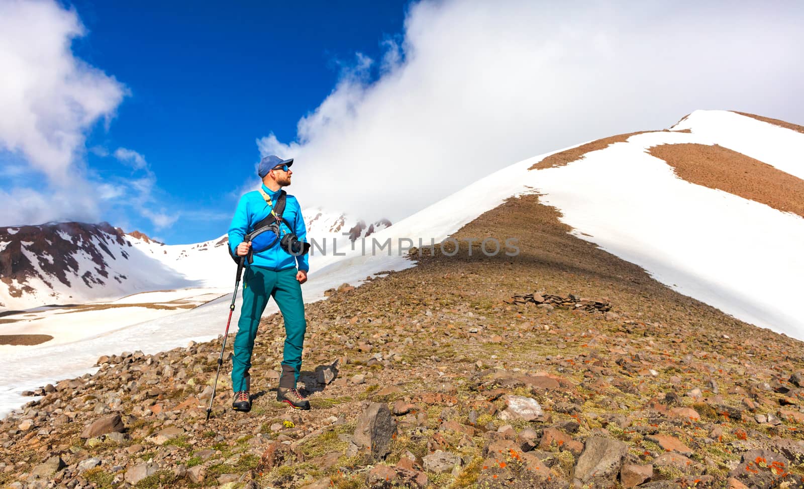Climber photographer with a camera over his shoulder peering at the top of a snow-capped mountain. by Sergii