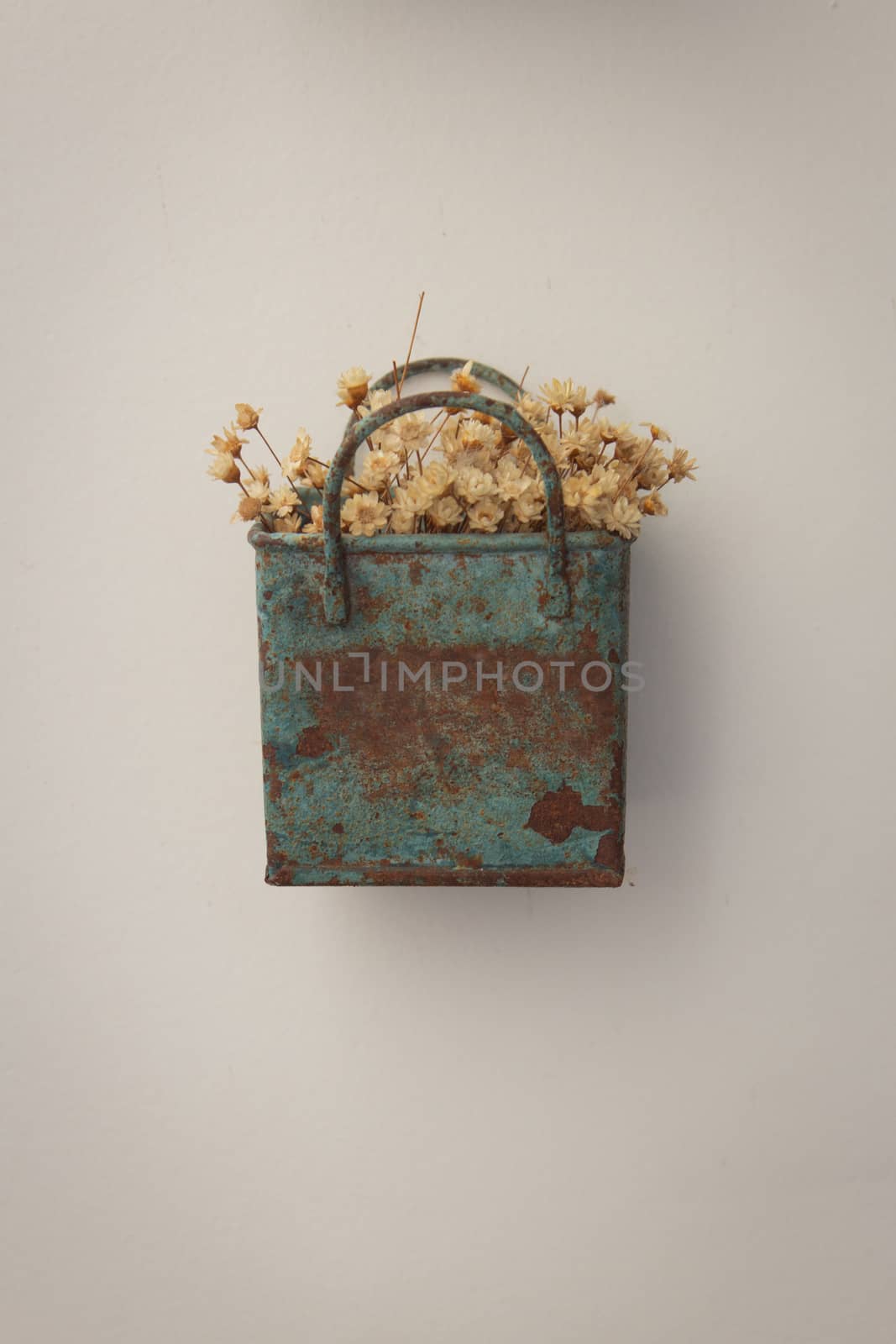 Bunch of tinny artificial flowers, hay colored, inside a blue metal box, very old and rusted, hanging on the wall