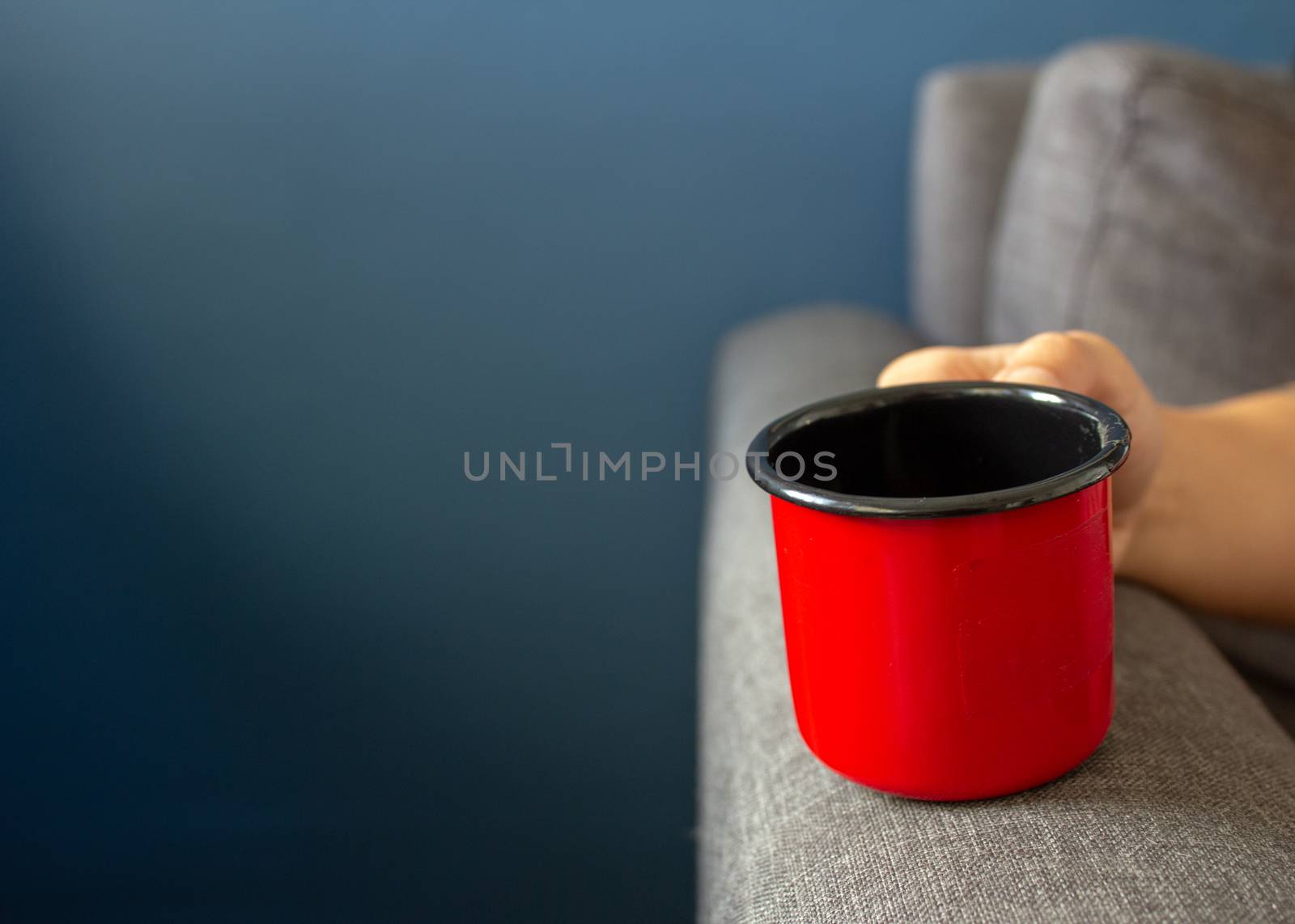 Woman holding a red metal cup resting her hand on the sofa's arm