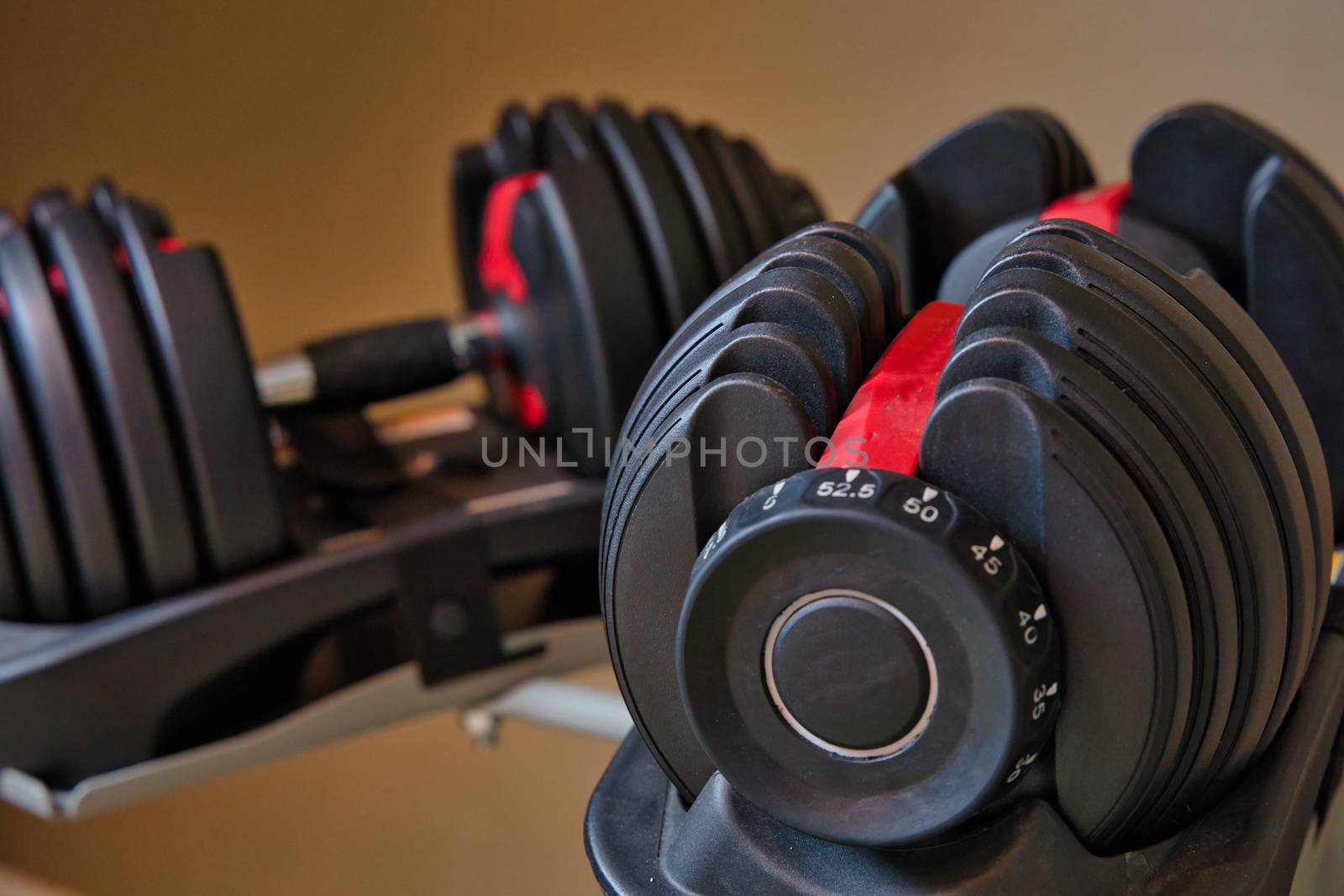 Set of adjustable dumbbells isolated on tan and brown background. Weights for working out at home.