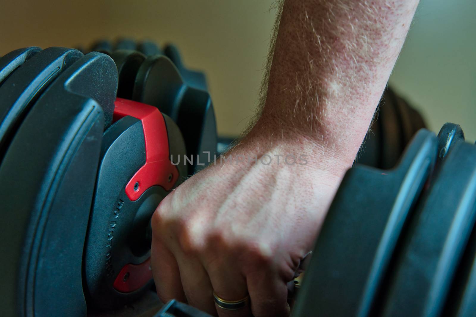 Hand gripping adjustable dumbbells for working out at home. male hand with ring visible.