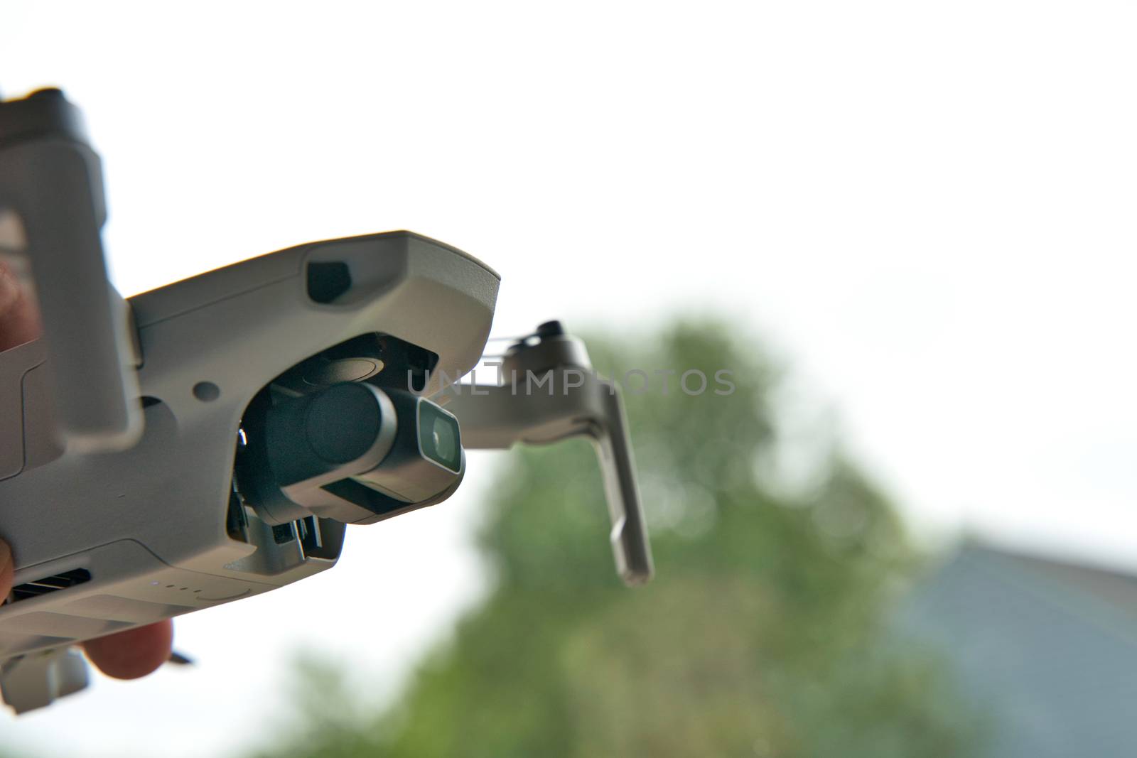 Underside of drone in flight. Tree and sky visible in background. Small drone product picture. Flying drone in house