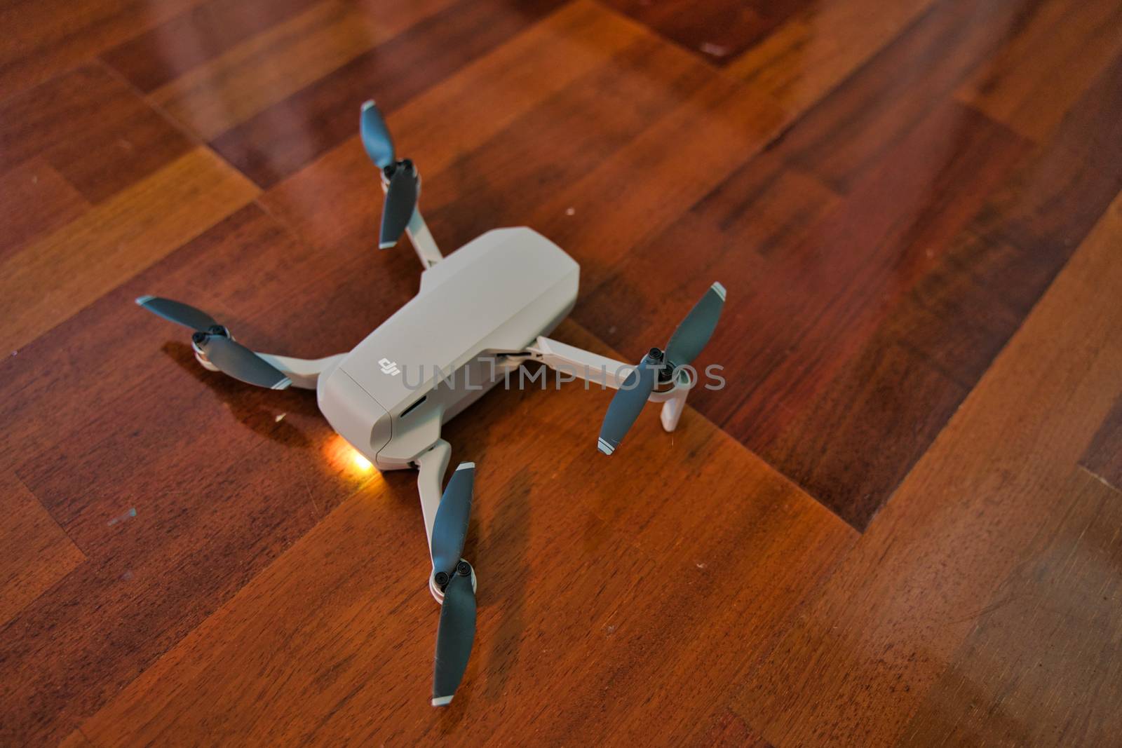 Drone sitting on wooden floor with light on indicating dead battery. Indoor drone flying.
