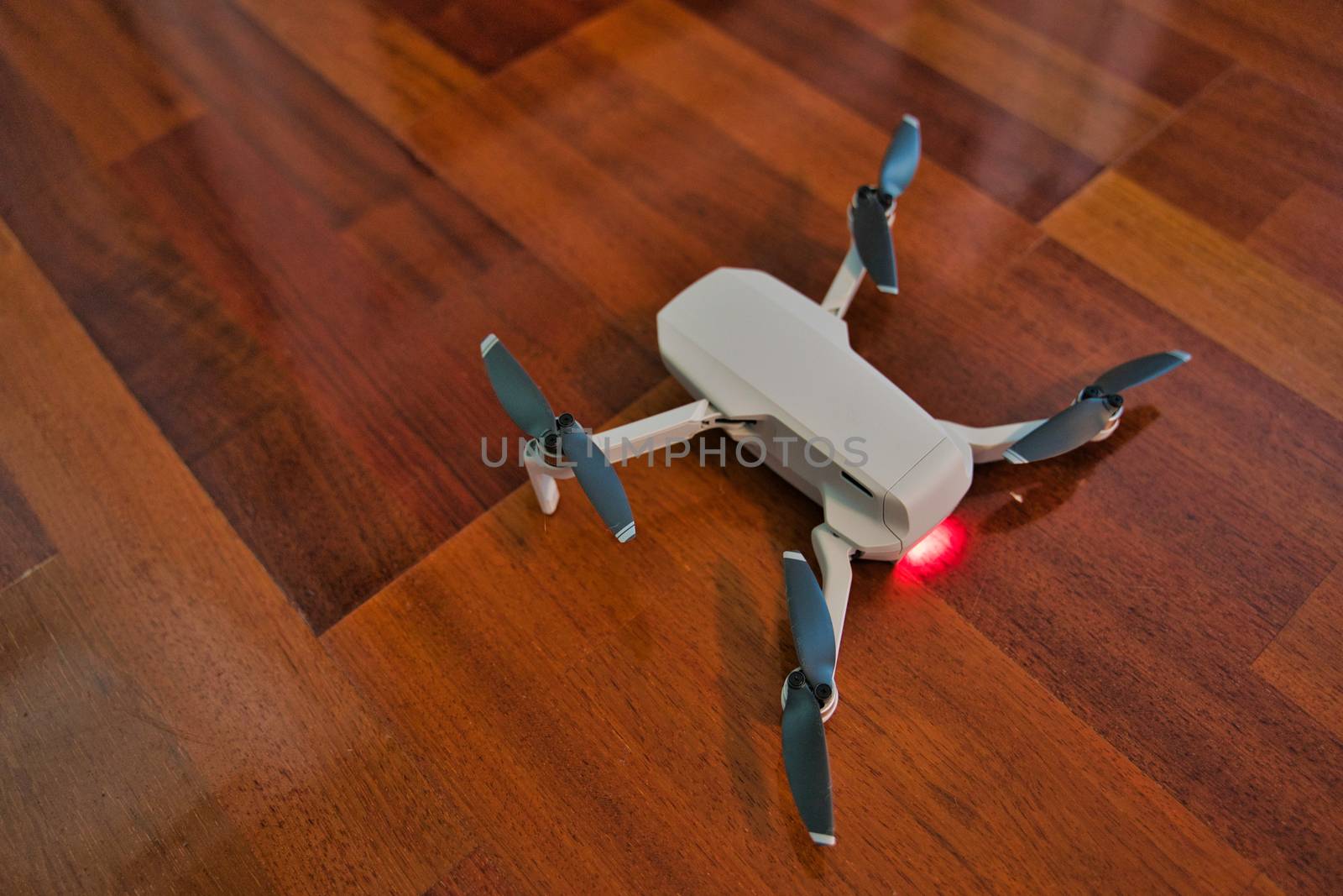 Drone sitting on wooden floor with light on indicating dead battery. Indoor drone flying.