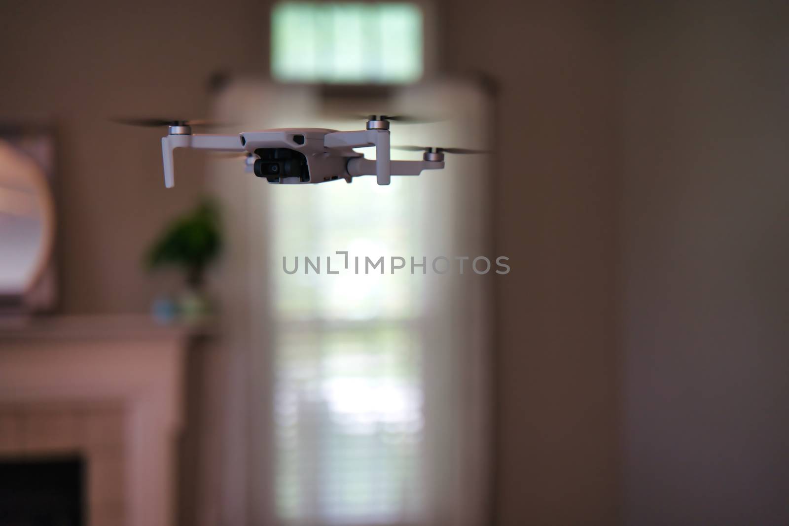 Drone flying indoors with window visible in background. White drone hovering inside of house.