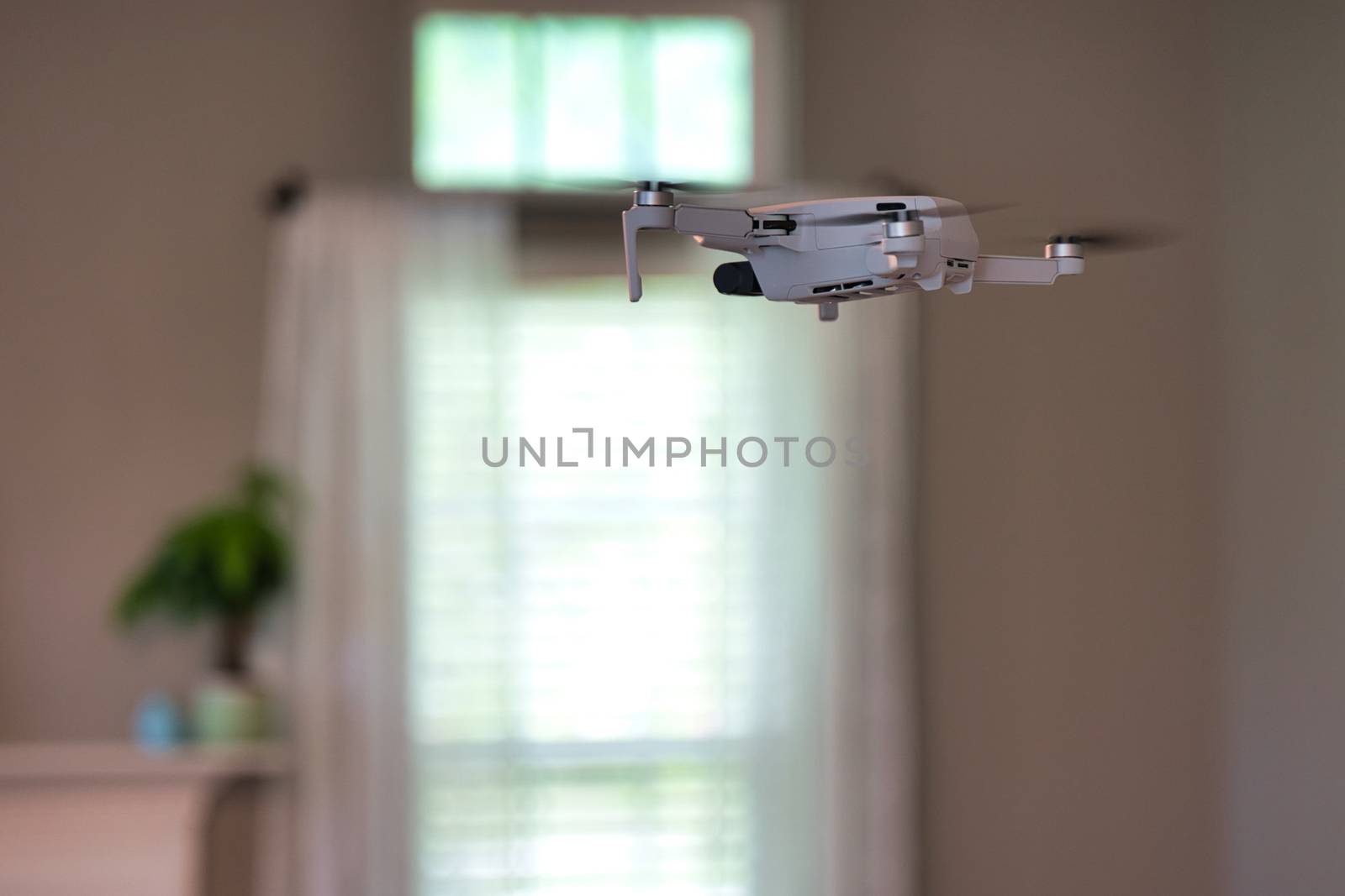 Drone flying indoors with window visible in background. White drone hovering inside of house.