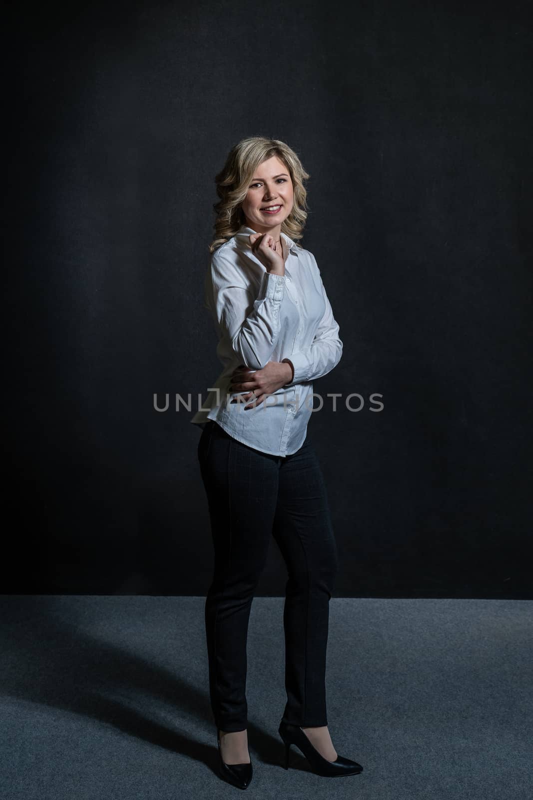 30 years old woman with blond hair in a white shirt posing in the studio on a dark background