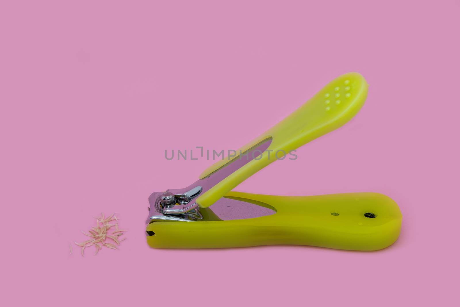 A Stainless Steel with green plastic handle Nail Clippers and some nails isolated on pink background.