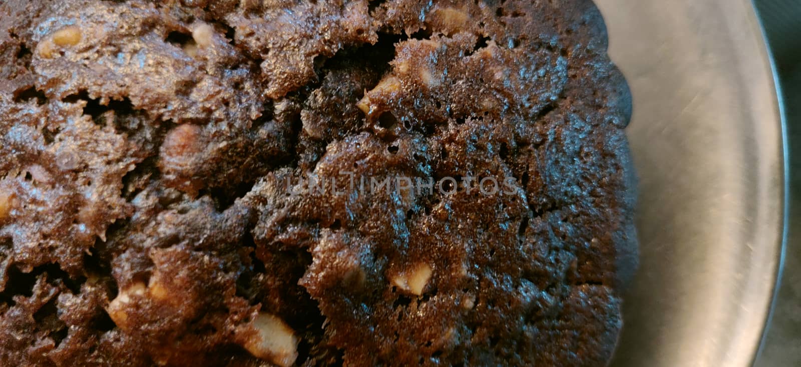 An extreme close up of hot and big chocolate walnut muffin on a steel plate on a weave pattern table