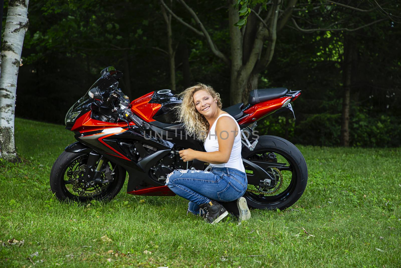 Young blond woman, kneeling beside a sport motocyle