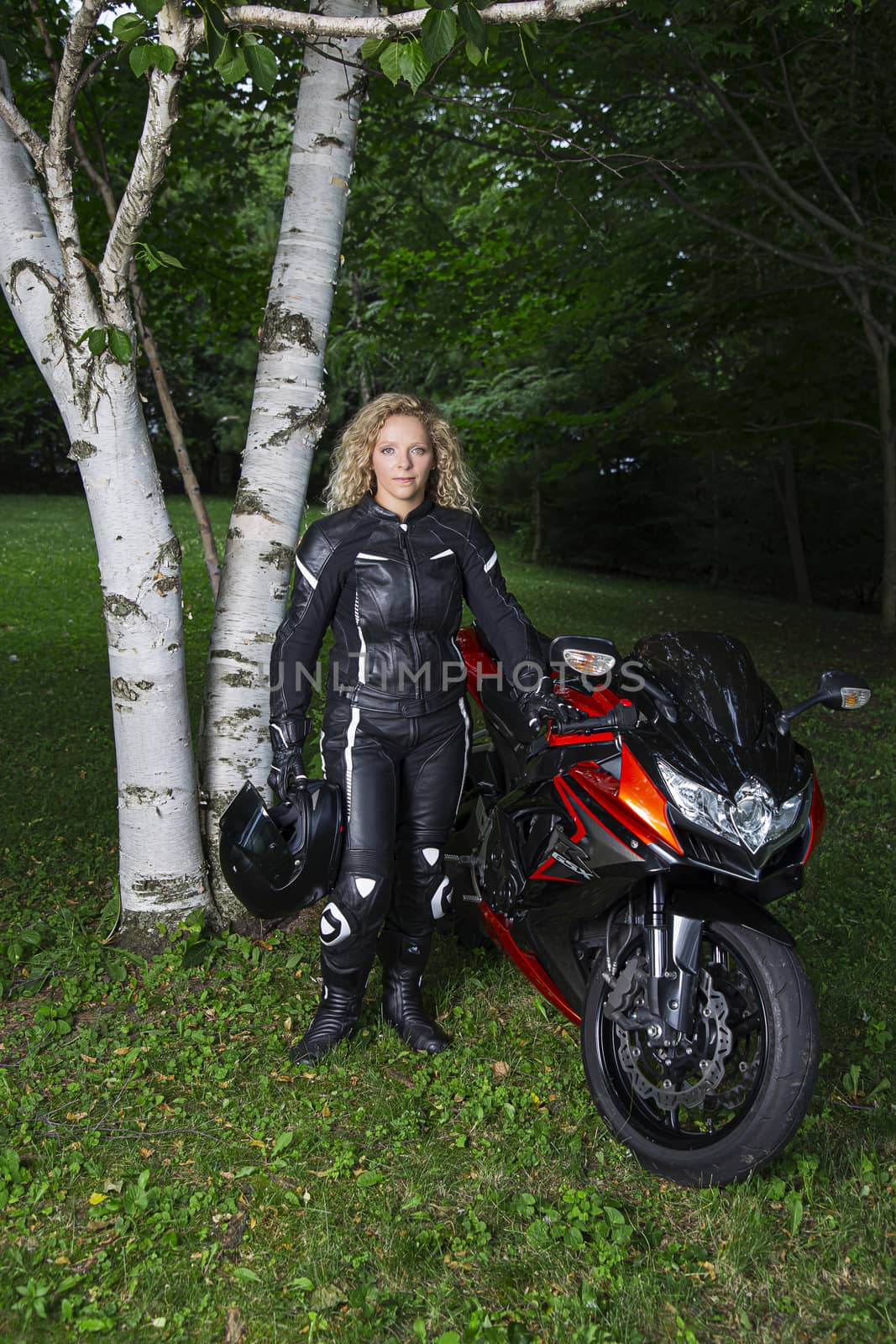 mid-twenties blond motocyclist woman, in full gear, standing beside her motocycle