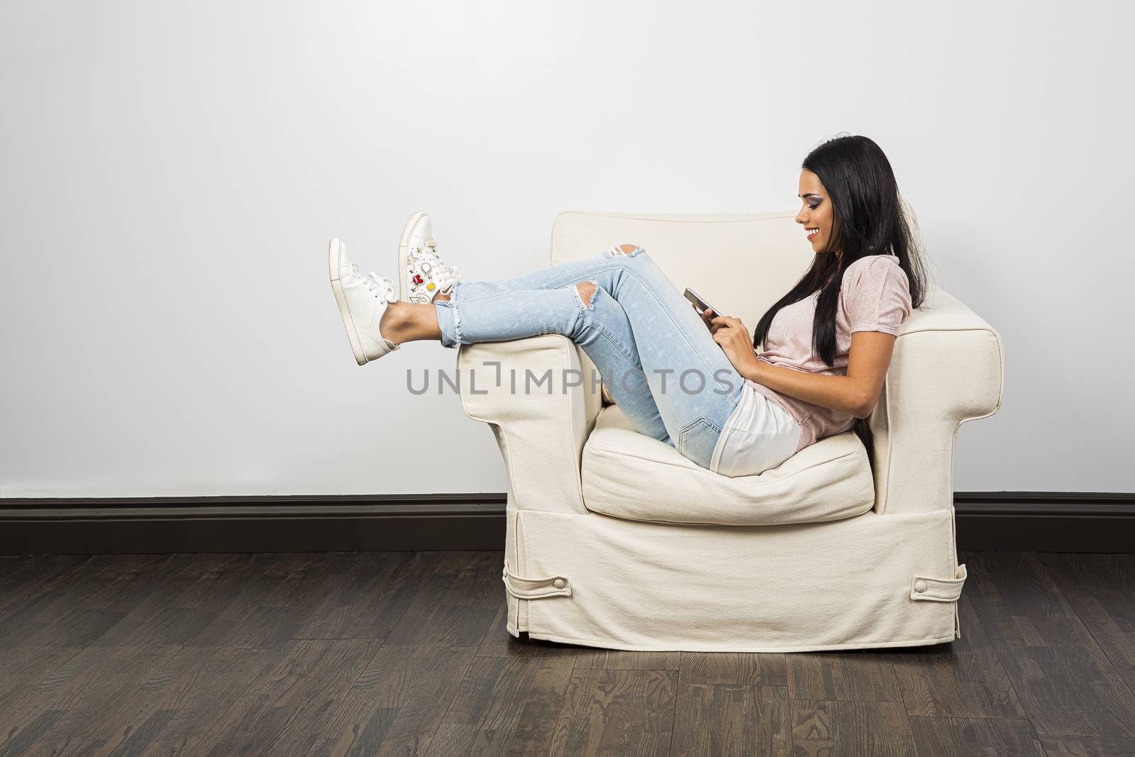Young woman with her leg up on the arm of the chair, looking at her phone