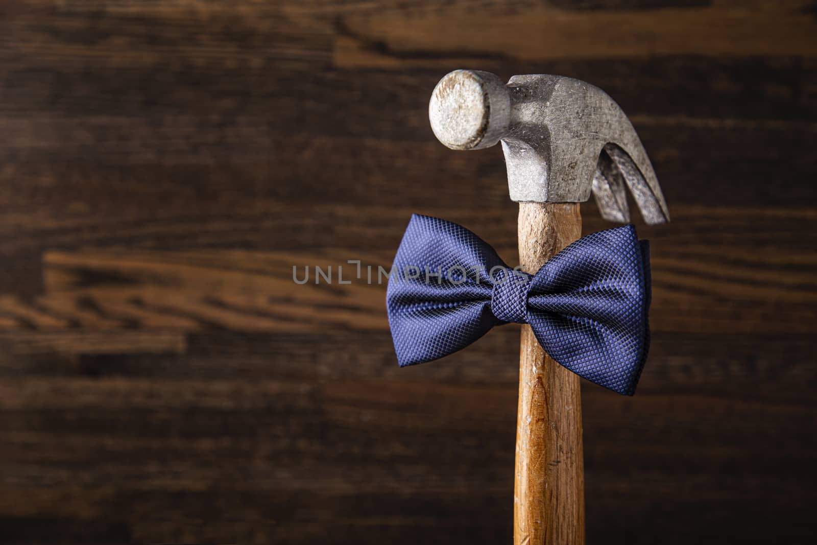 Old banged up hammer with a blue bowtie against a wood background