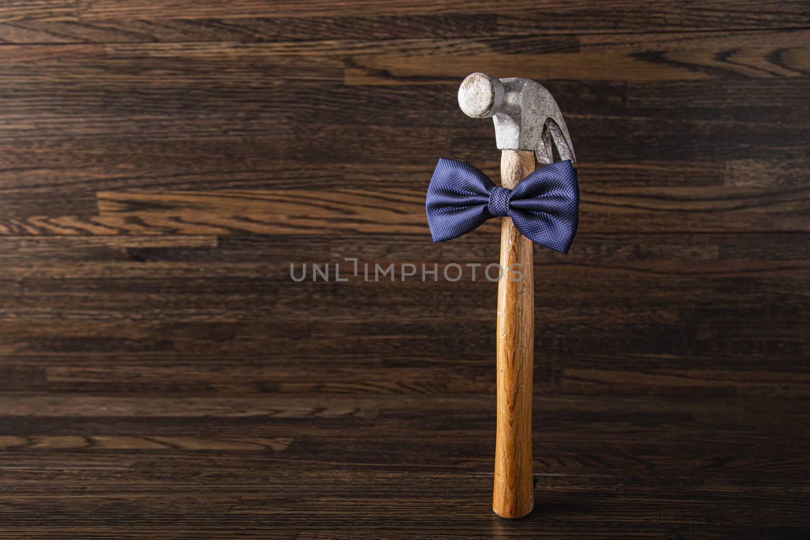 Old banged up hammer with a blue bowtie against a dark wood background