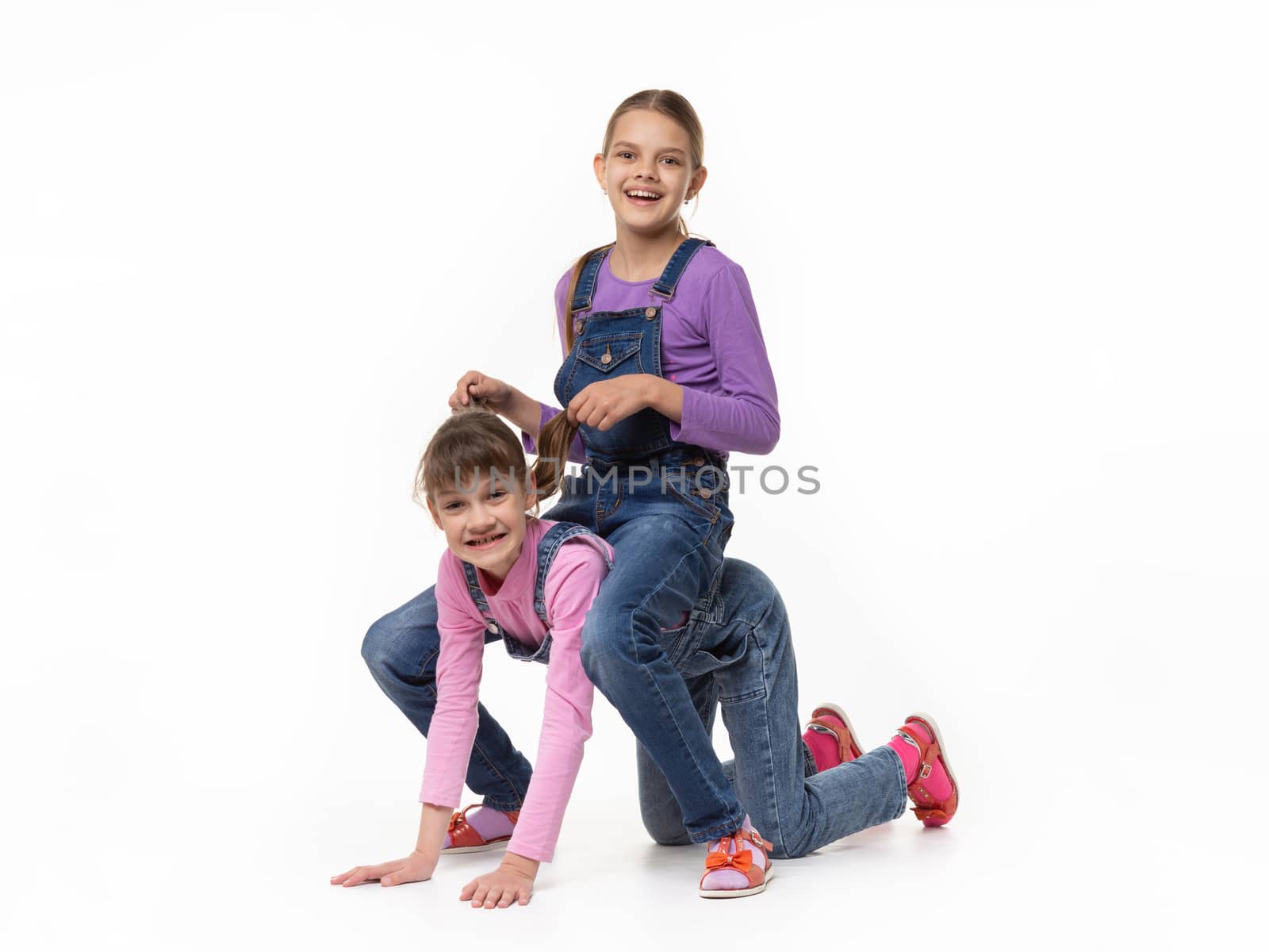 Two sisters play jockey and horse against a white background