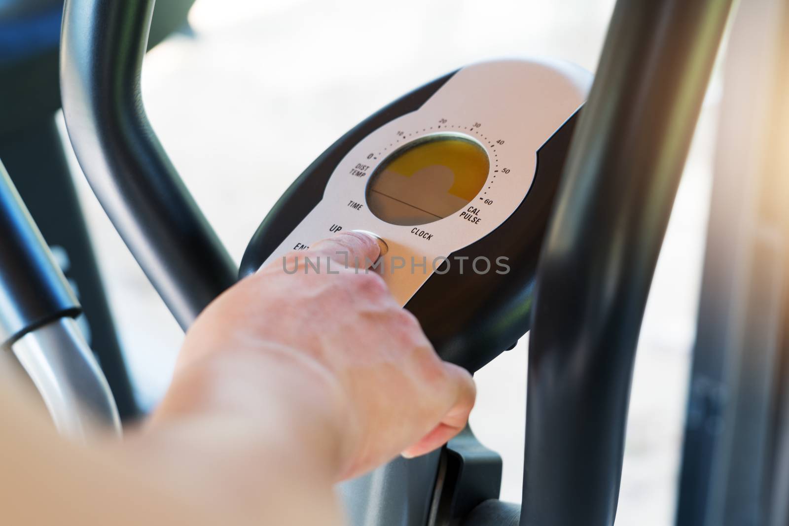 finger pressing on button of elliptical bike machine in fitness gym