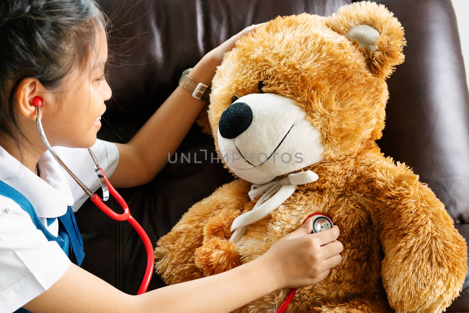 little girl is smiling and playing doctor with brown bear and stethoscope. Kid and health care concept.