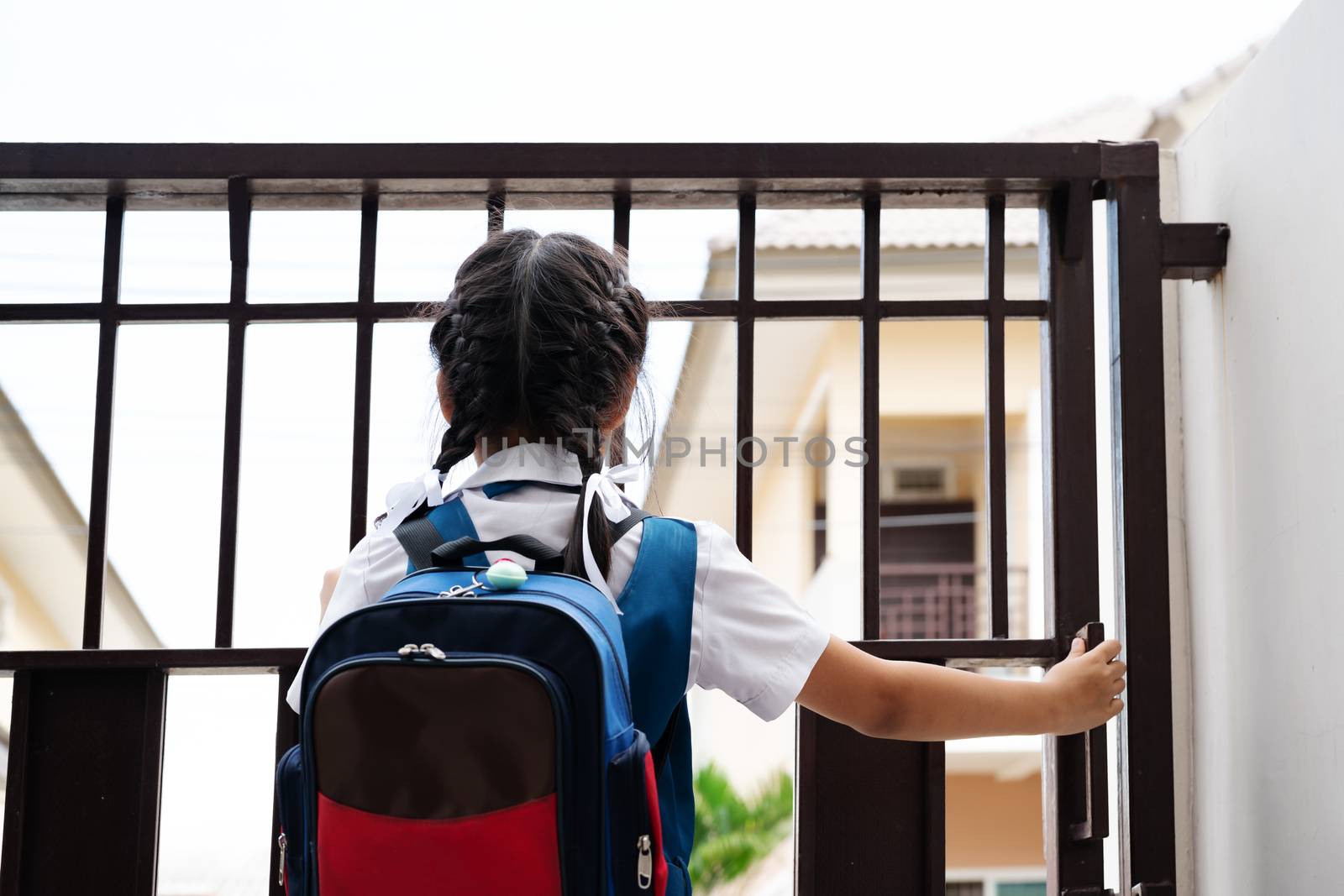 Little asian girl in uniform opening the door for leaving to school in the morning with blue back pack