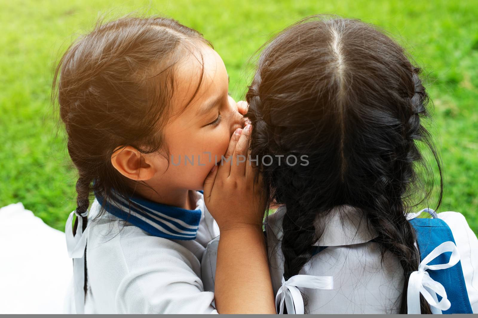 Two young girls whispering and sharing a secret during playground session on green glass background