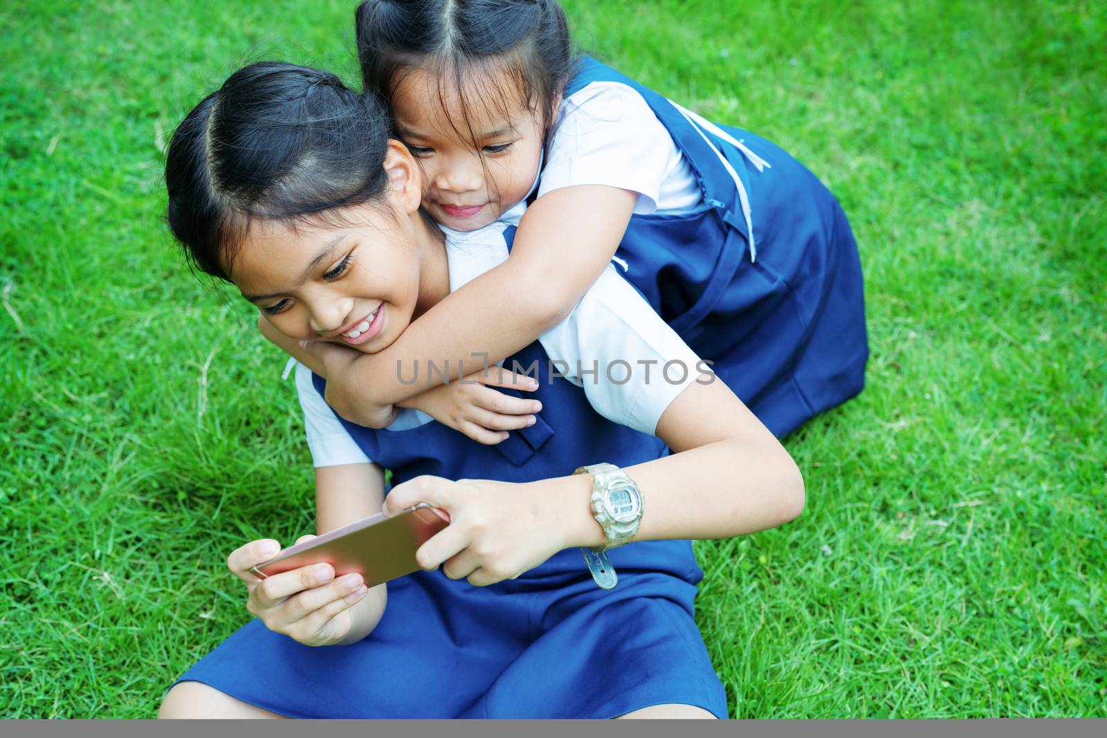 two little sister girls playing internet with mobile smartphone on grass