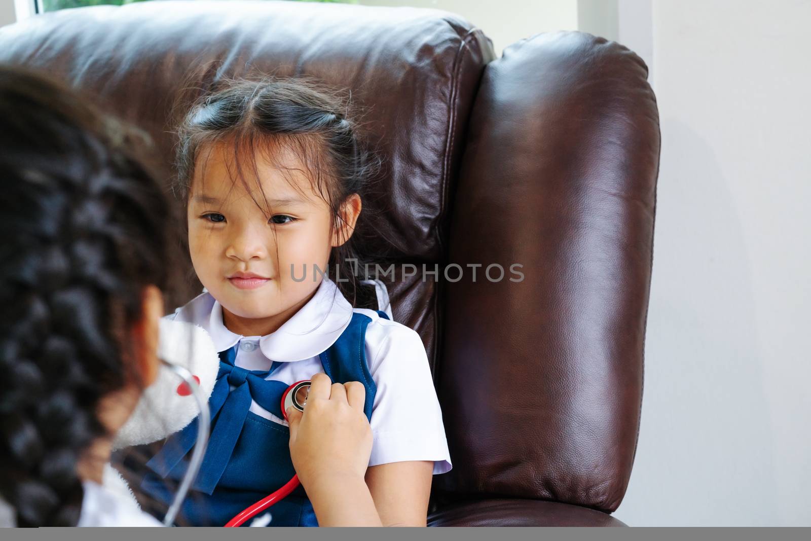 two little girl are smiling and playing doctor with stethoscope. by psodaz