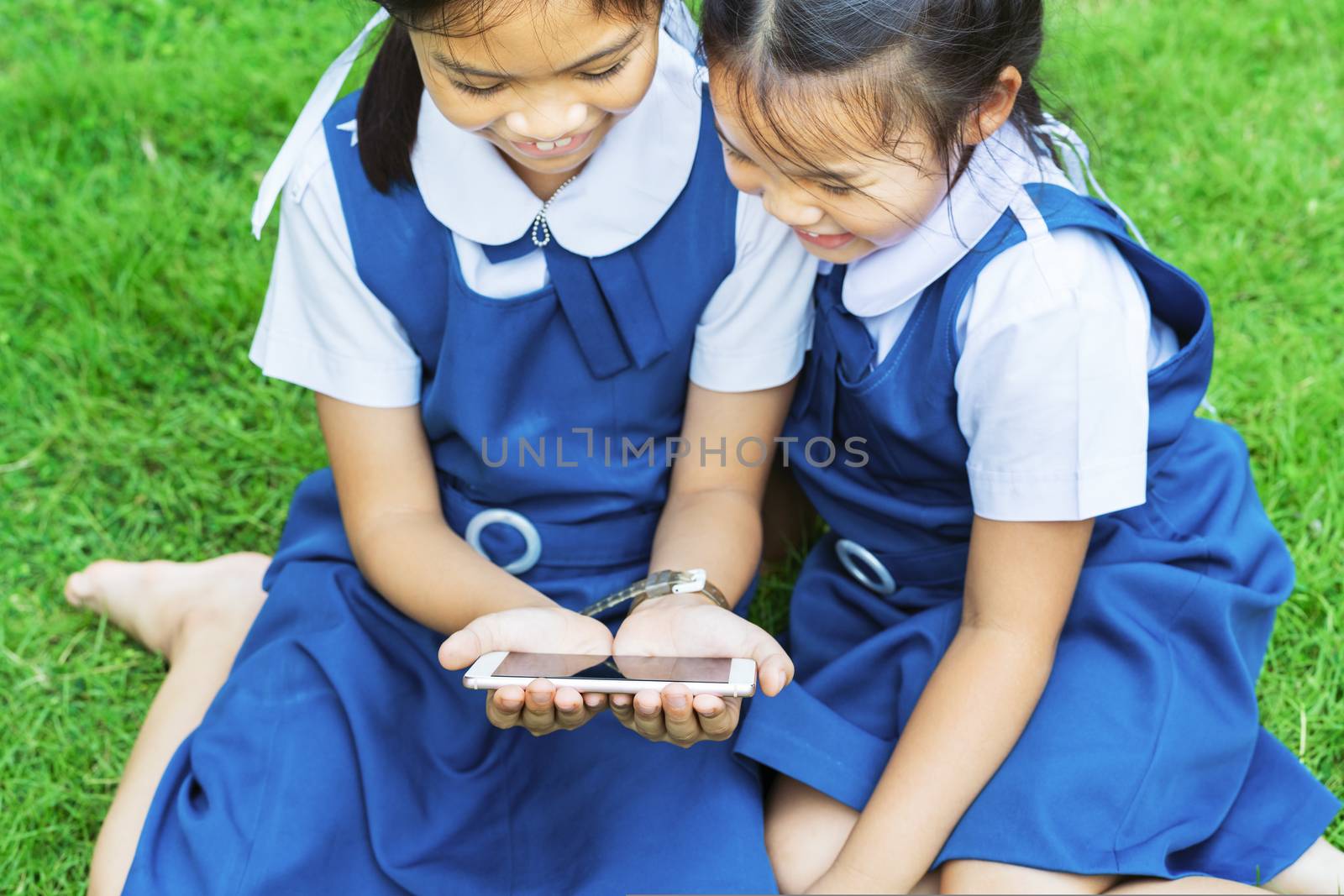 two little sister girls playing internet with mobile smartphone on grass