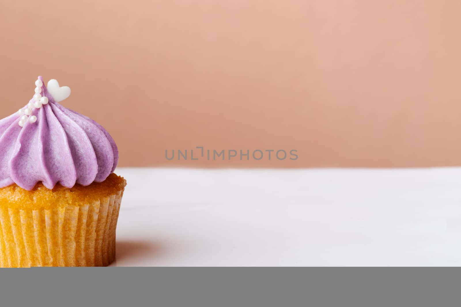 cute cupcake with small white heart on purple cream on pink background