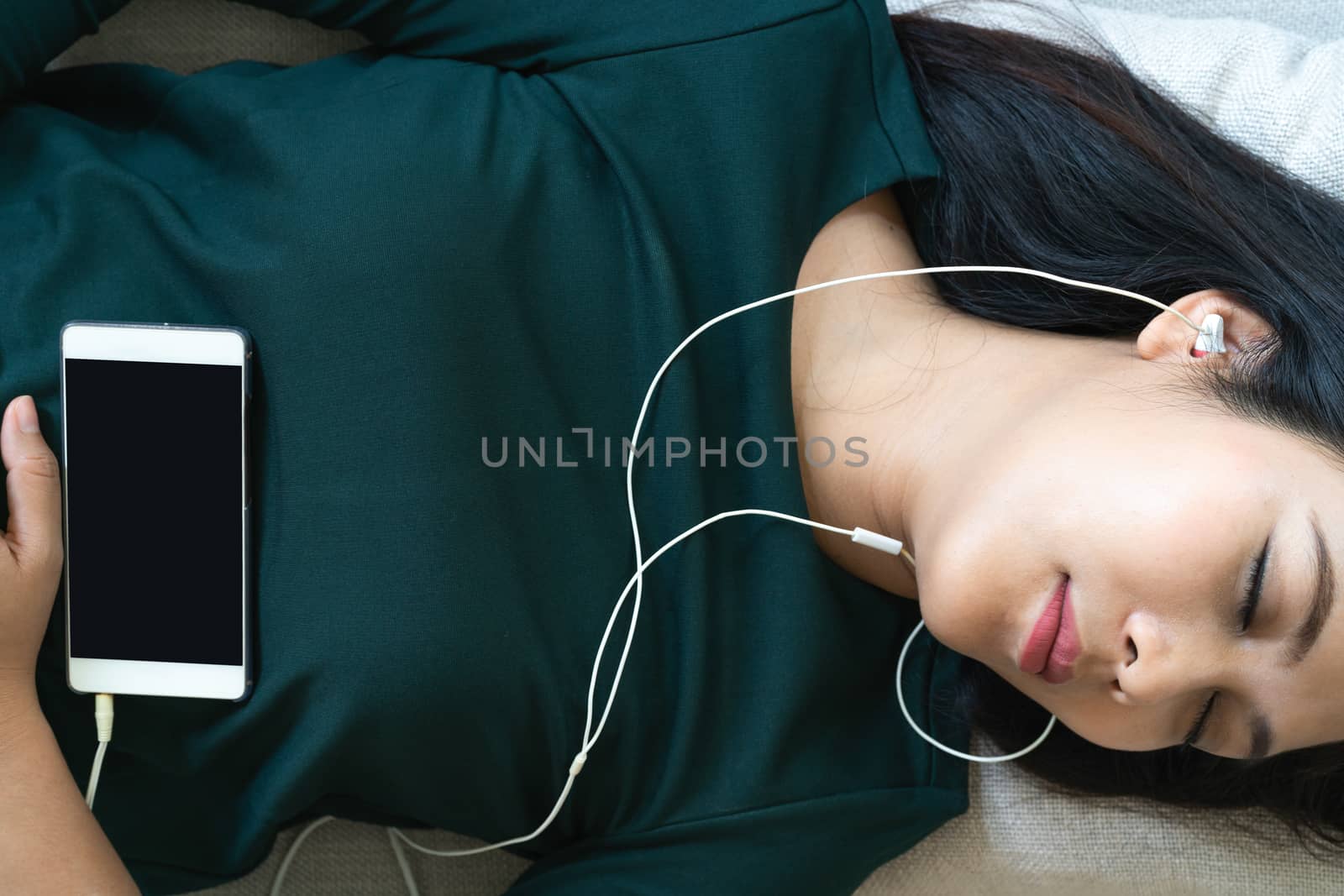 Over head view of beautiful young woman laying down on sofa using smartphone to listen the music