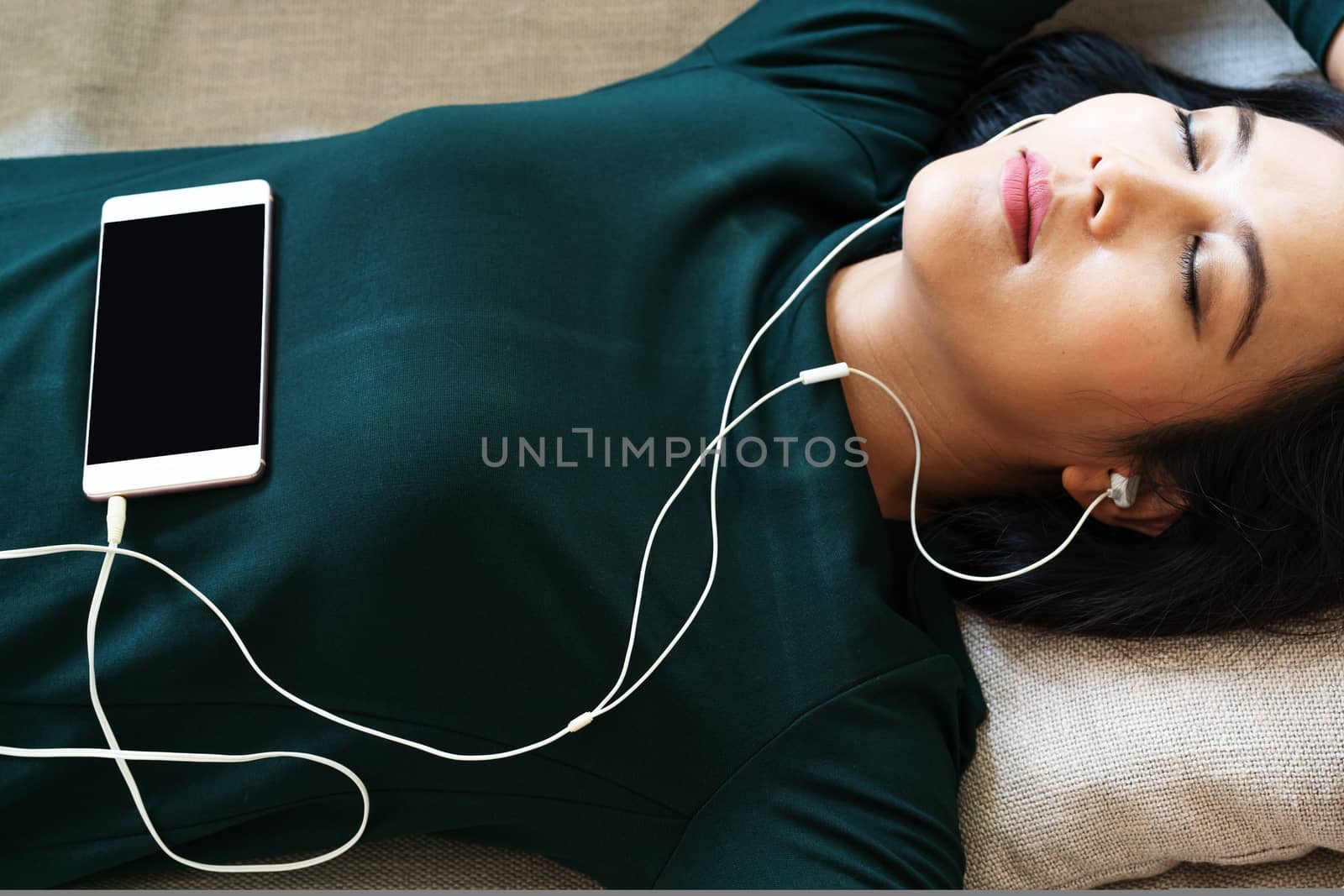 Over head view of beautiful young woman laying down on sofa using smartphone to listen the music