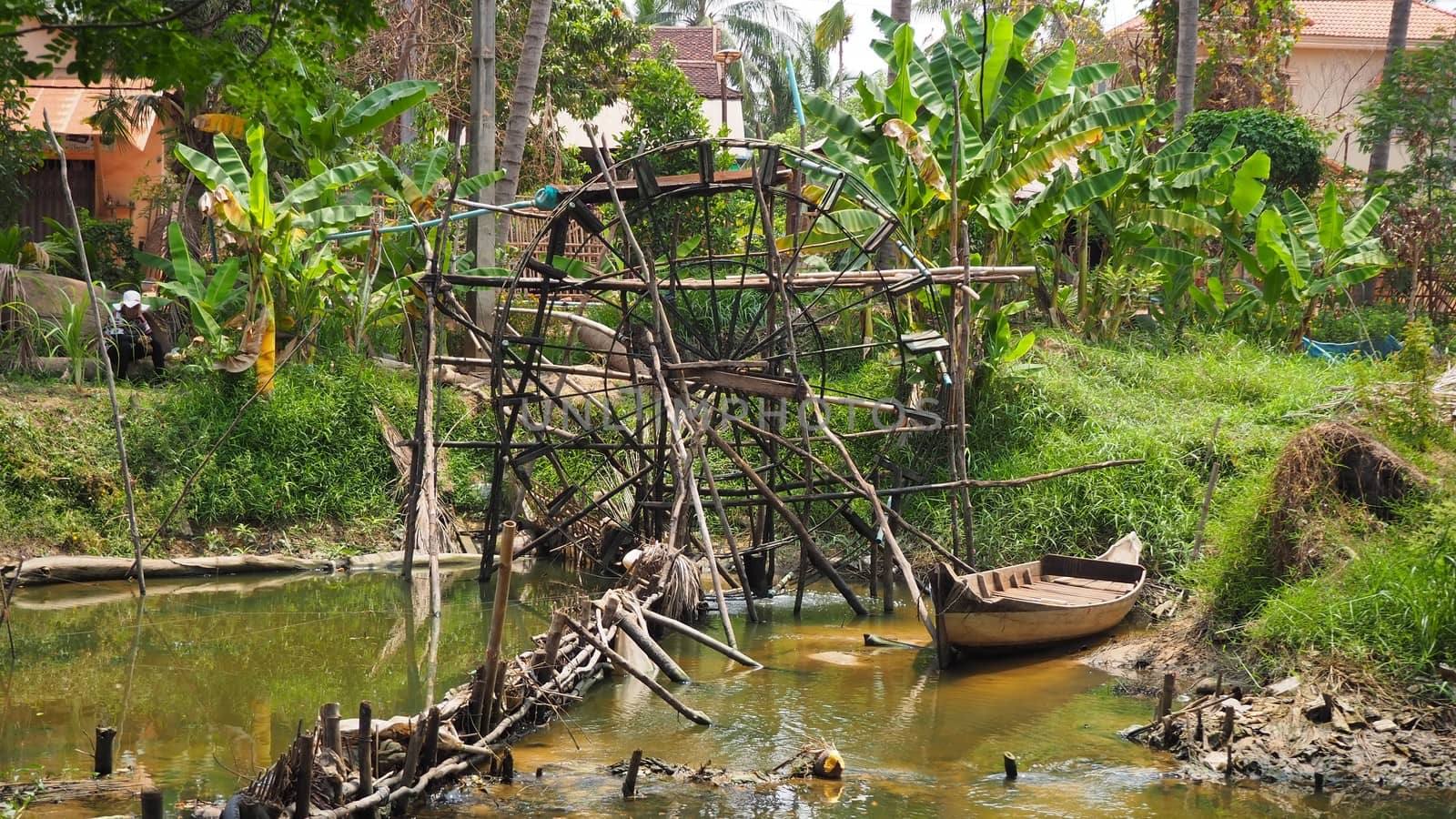 a boat next to a water wheel pump in the river in siem reap cambodia by AndrewUK