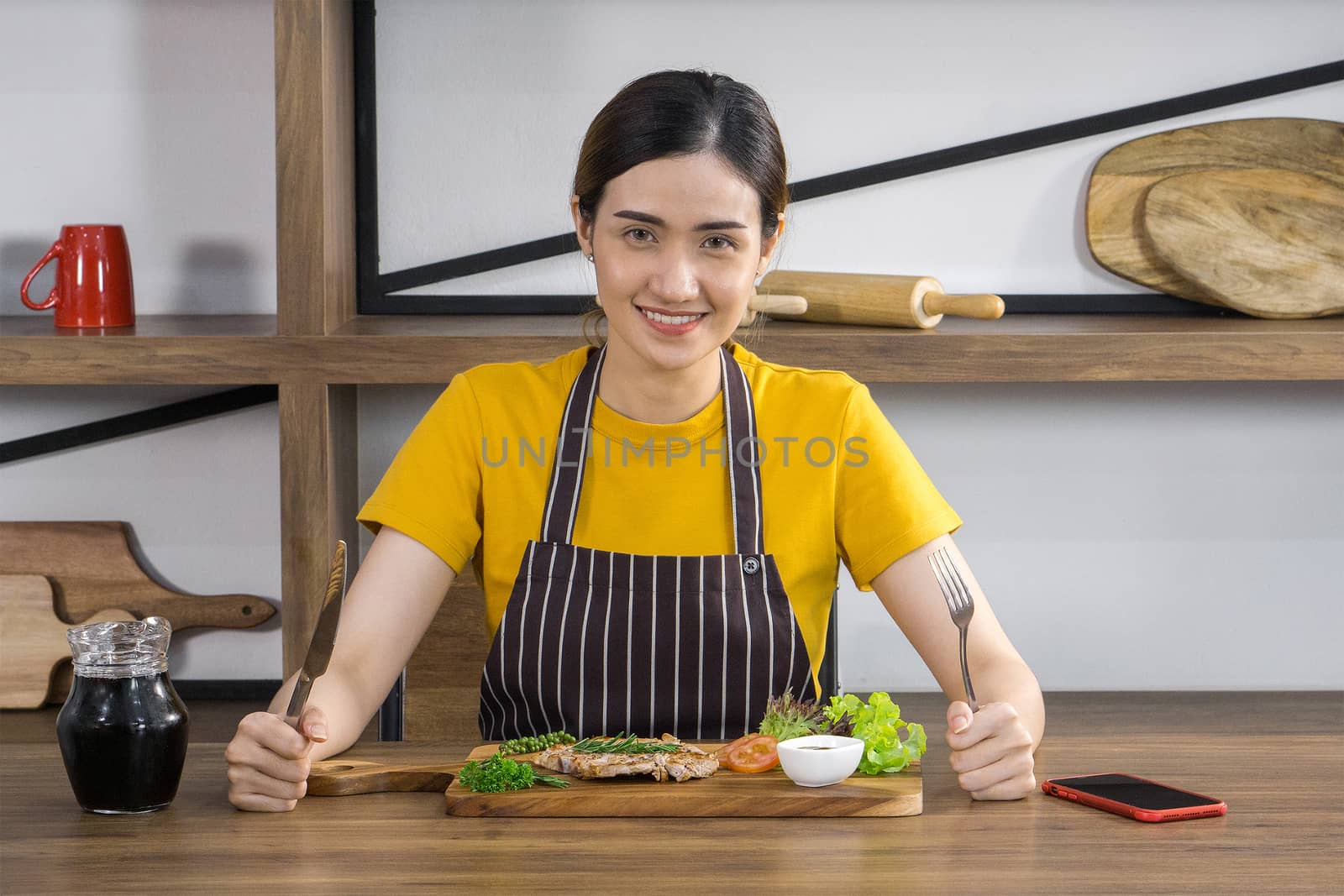 The housewife dressed in an apron, prepared a fork and knife, ready to eat a delicious steak. Morning atmosphere in a modern kitchen