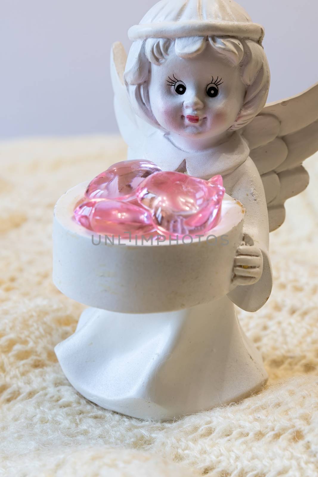 White ceramic figurine of an angel holding a basket with pink hearts, on a light background. Angel figurine for concept design. The concept of love and kindness.
