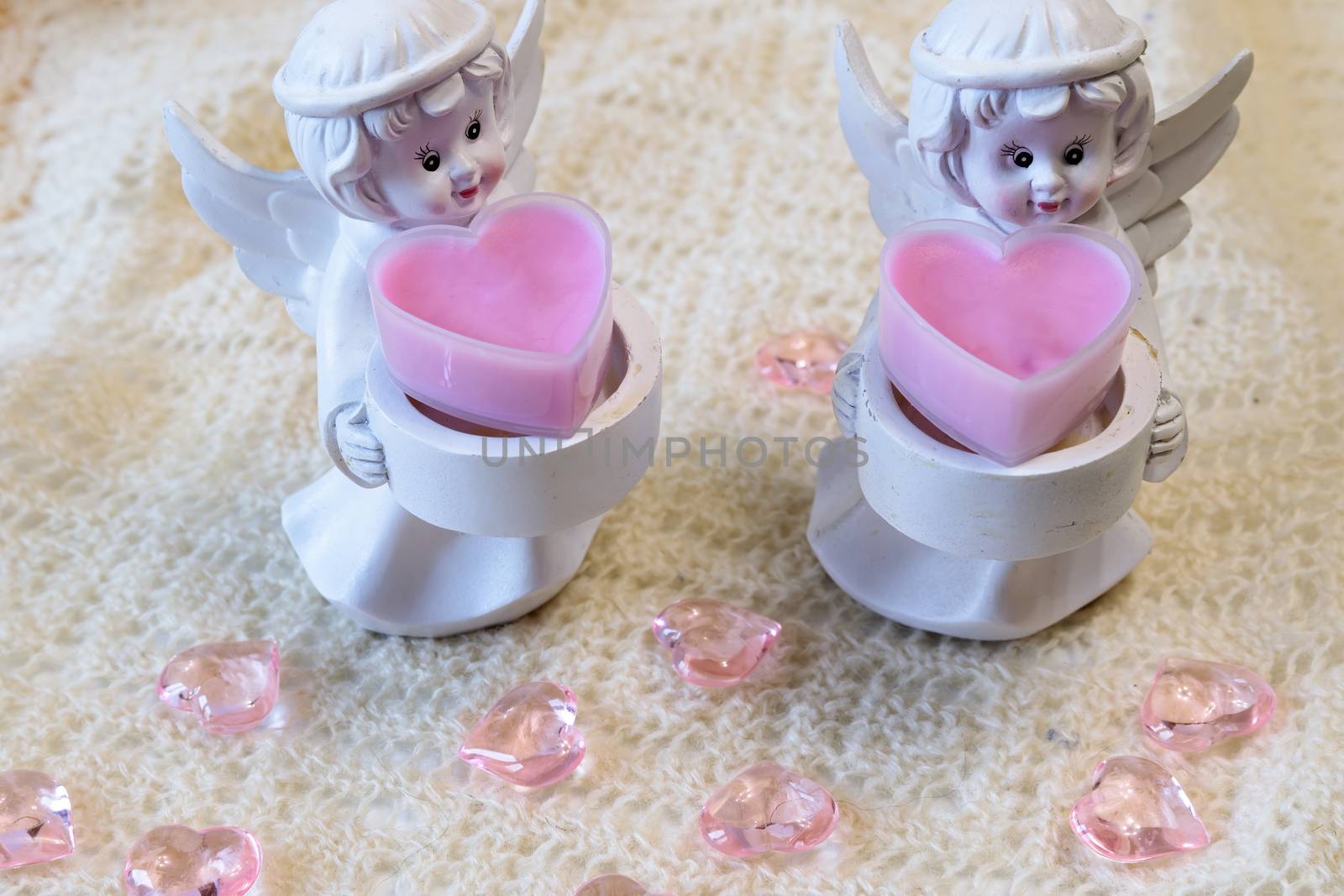 Two white ceramic angel figurines with baskets with pink hearts on a light background. Angel figurine for concept design. The concept of love and kindness.